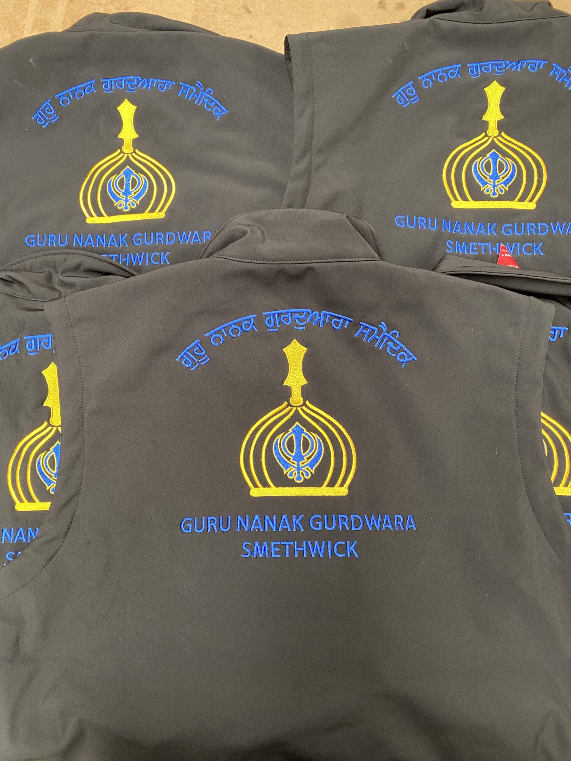 Five black gilets with embroidered logos. Each gilet features the logo for Guru Nanak Gurdwara based in Smethwick.