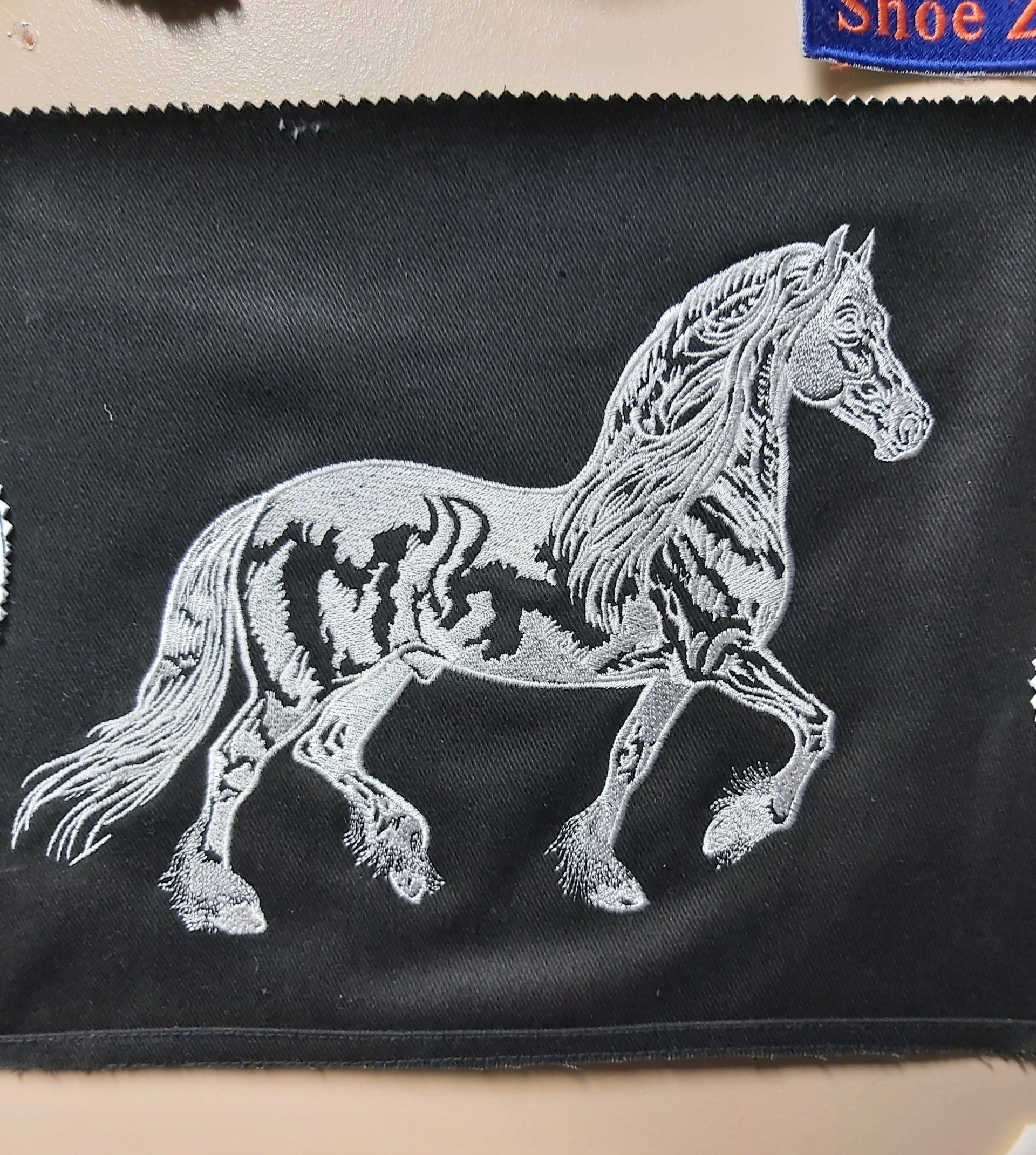Silver embroidered horse on black fabric. The horse is in profile, prancing.