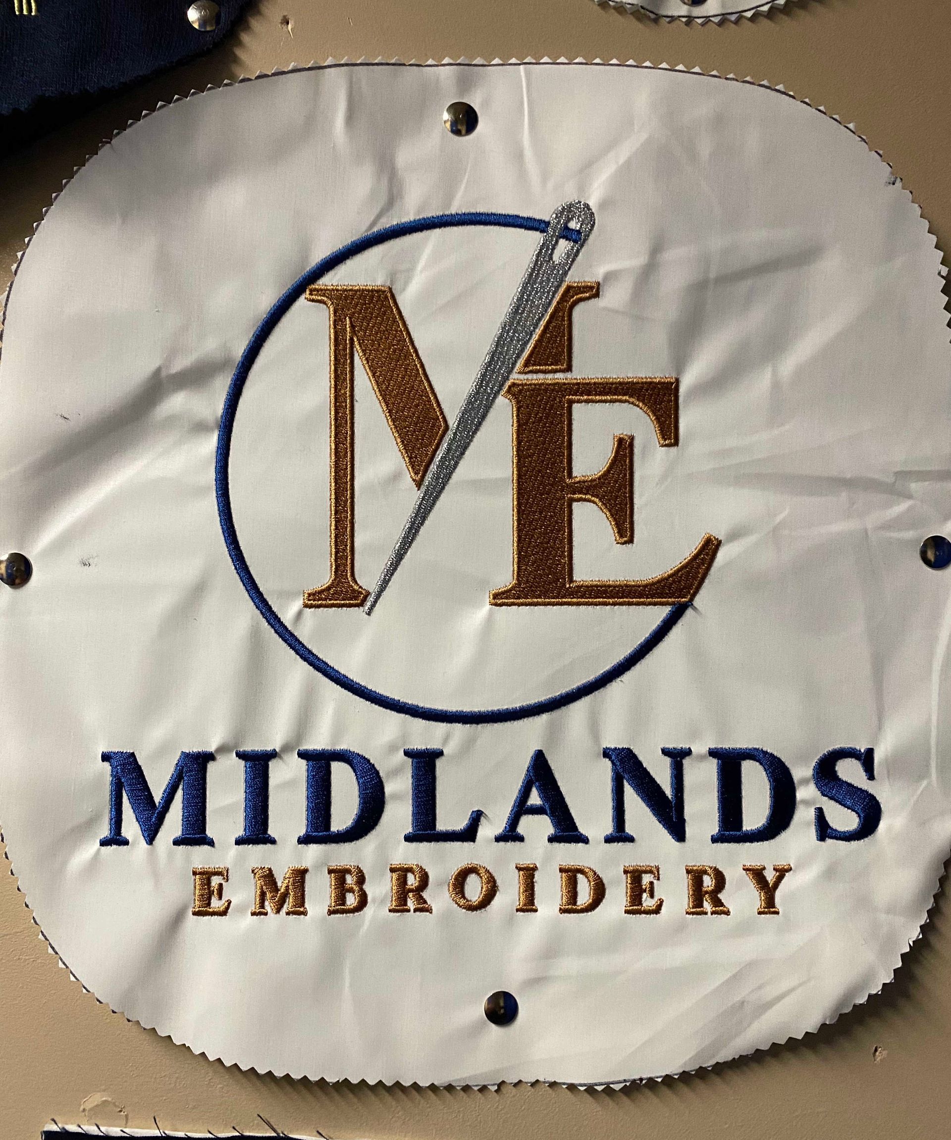 Embroidered logo for Midlands Embroidery: Blue and gold lettering, with an emblem of a needle and thread piercing the