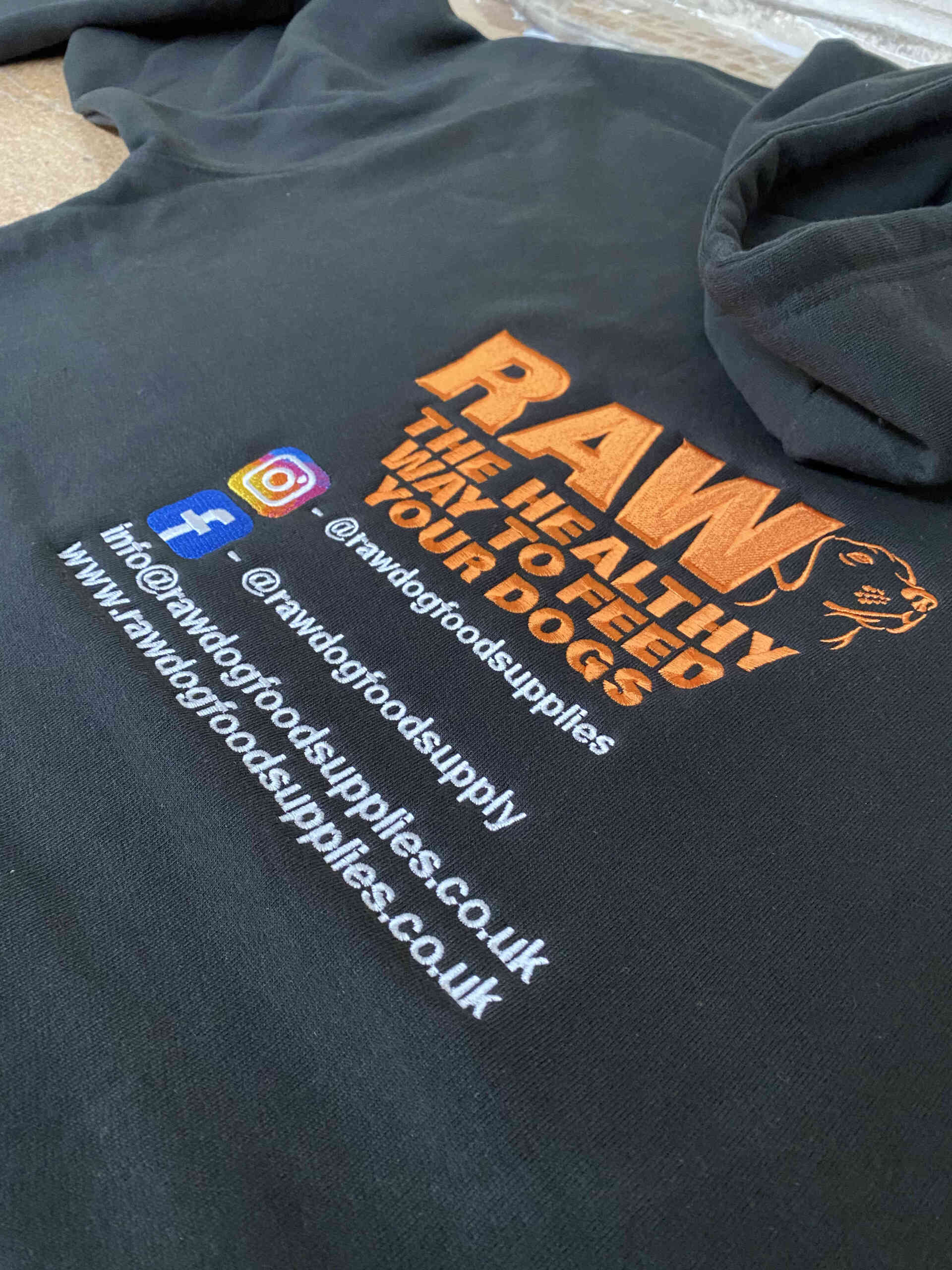 Black hoodie with an embroidered logo Contact information and social media icons are also present.