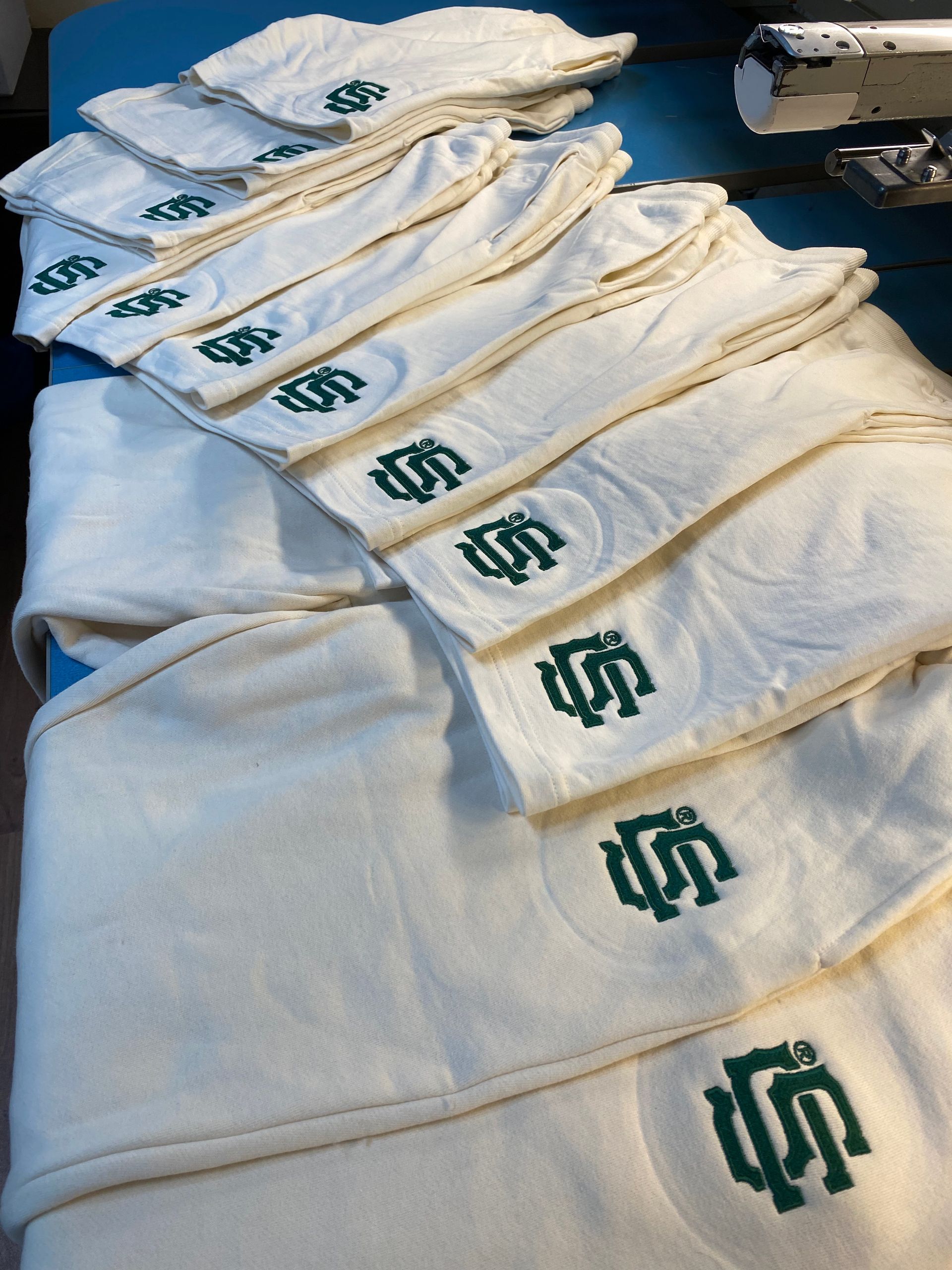 Off-white shorts and joggers with green embroidered initials. A few items are stacked on a light blue surface.