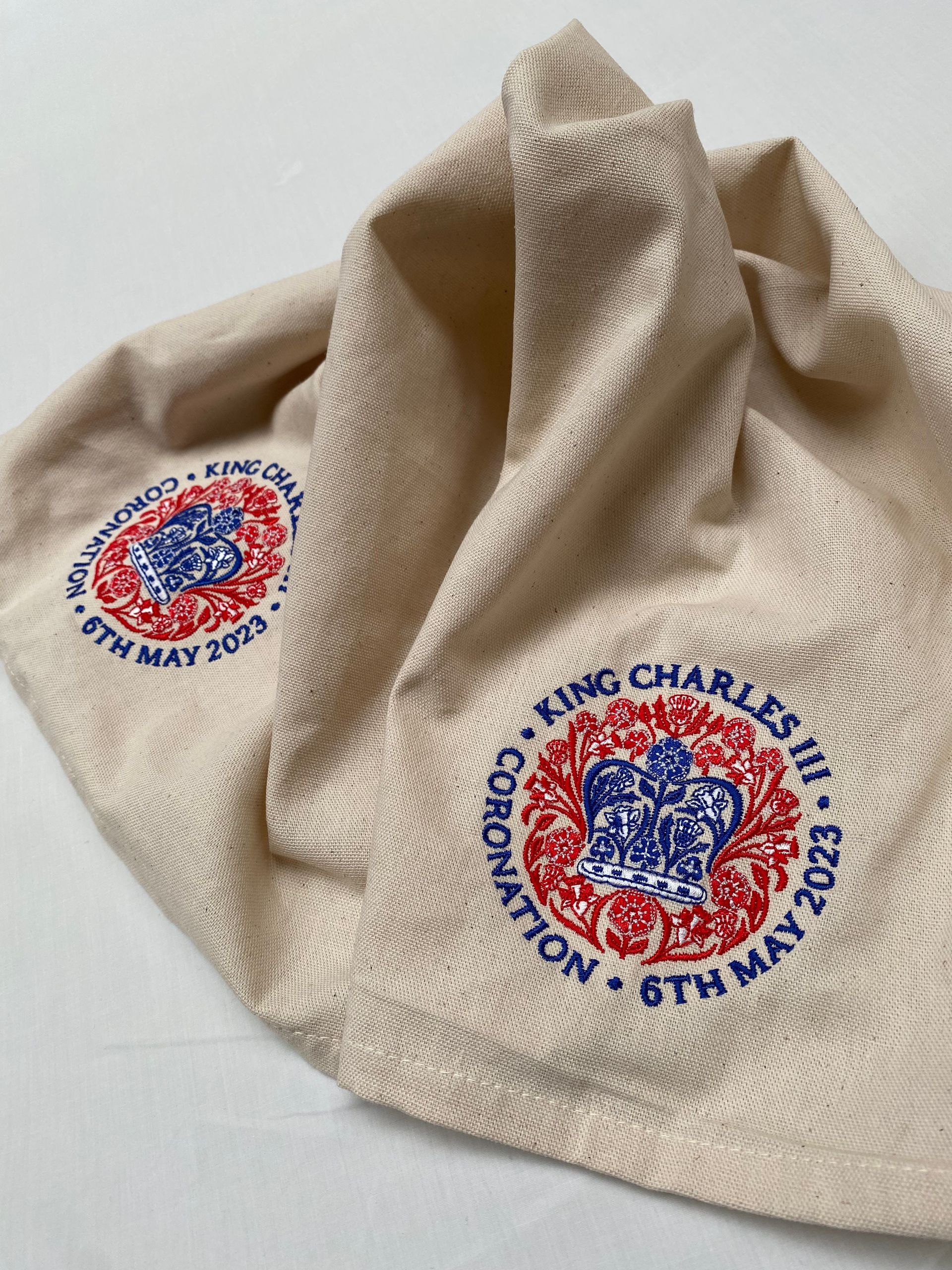 Tea towels with embroidered circular logos featuring the Royal crest and