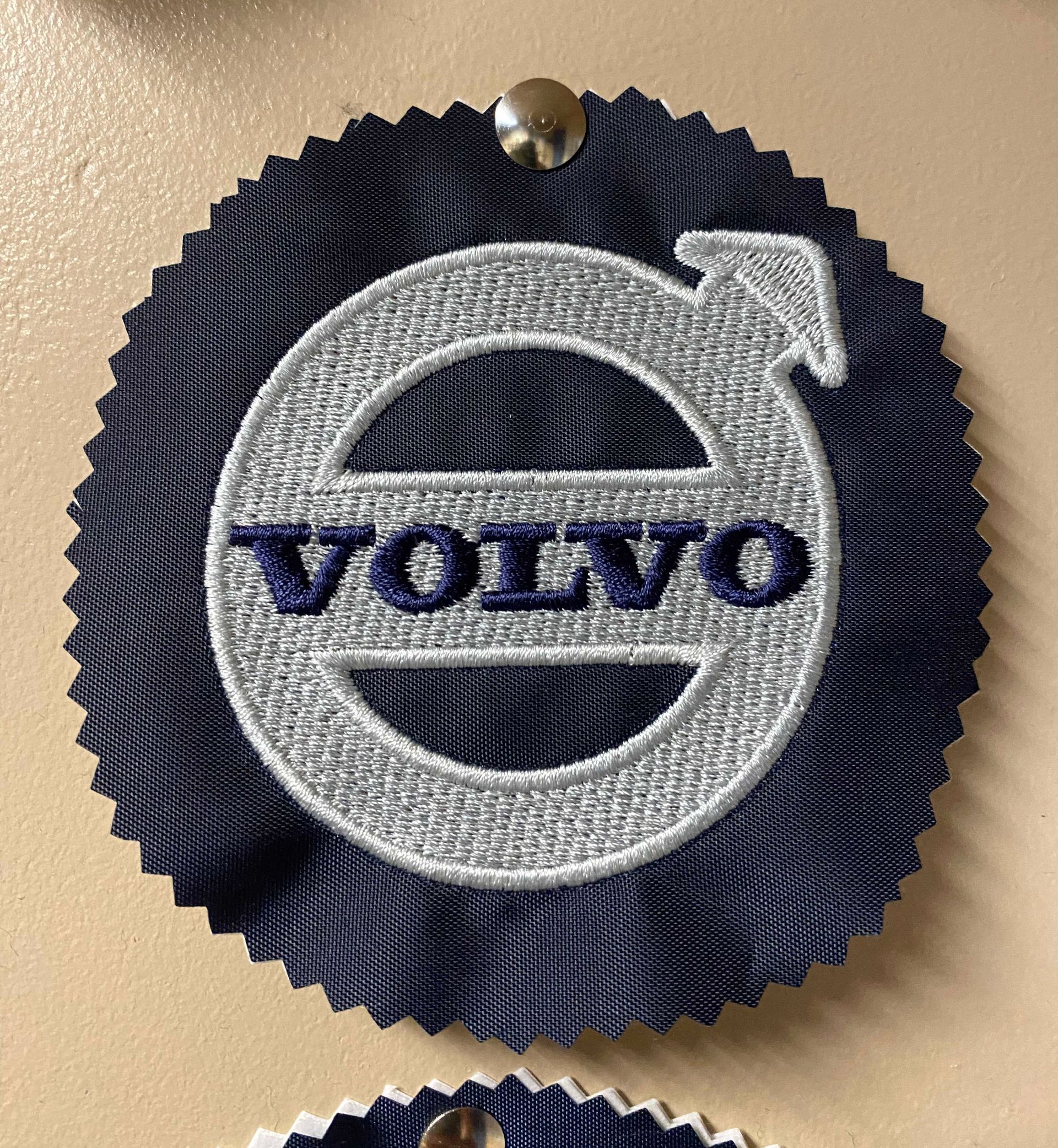 Blue Volvo logo embroidered on a navy rosette, pinned to a surface.