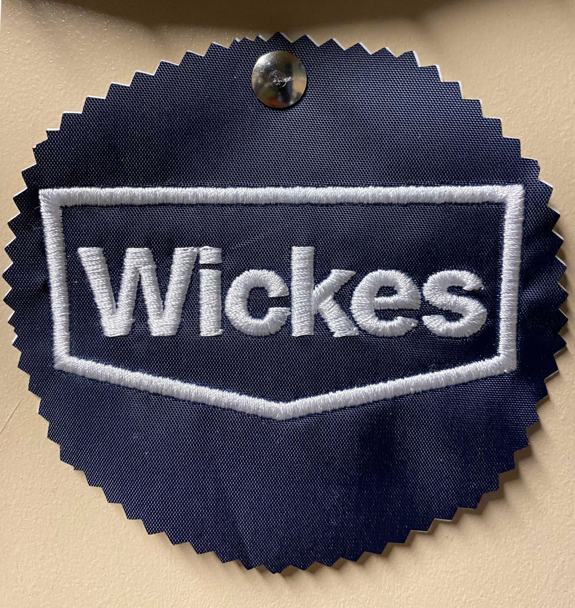 Dark blue rosette with a embroidered white Wickes logo, secured with a silver tack.