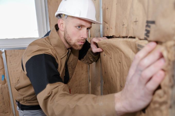 A man wearing a hard hat is working on a wooden wall.