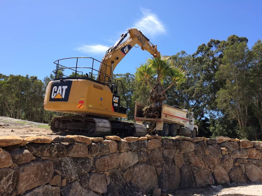 A Cat Excavator Is Working On A Stone Wall — J & M Bashforth & Sons In Brunswick Heads, NSW