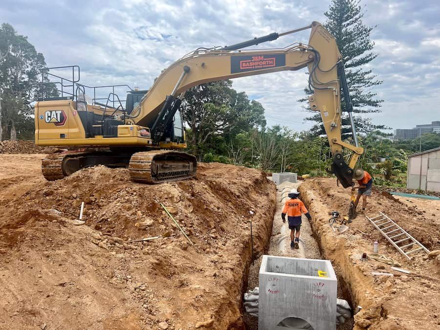 A Large Yellow Excavator Is Digging A Hole In The Dirt — J & M Bashforth & Sons In Brunswick Heads, NSW
