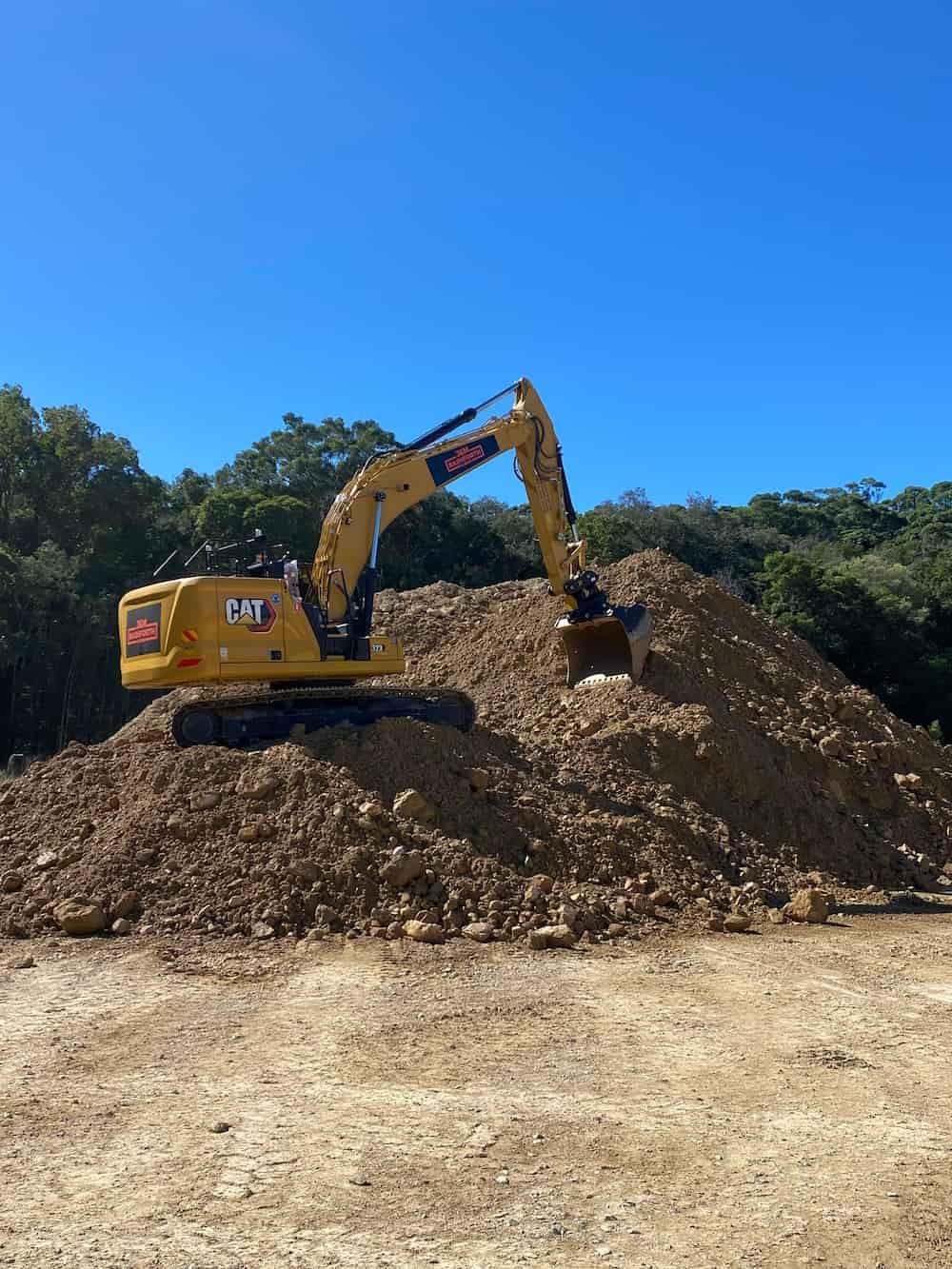 A Yellow Excavator Is Working On A Pile Of Dirt In A Field — J & M Bashforth & Sons In Brunswick Heads, NSW