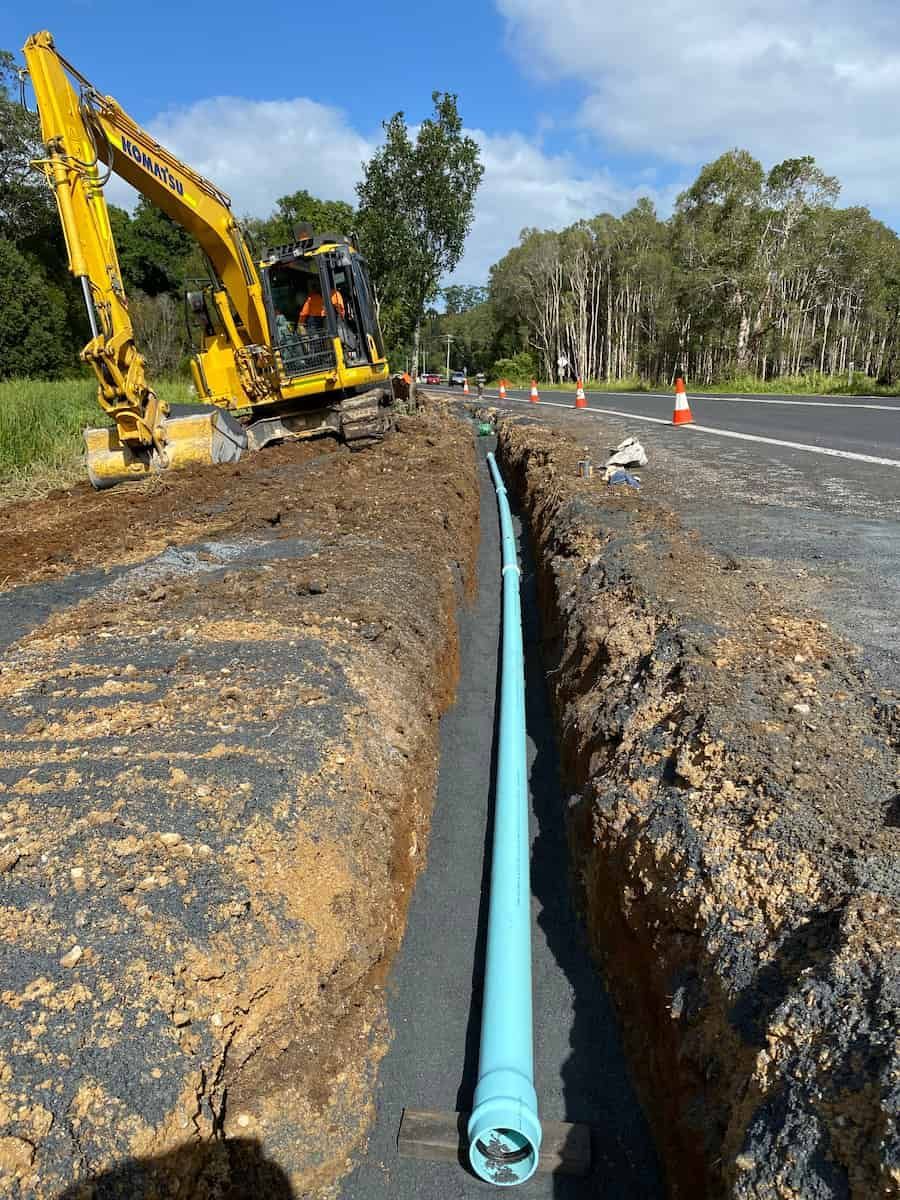 A Yellow Excavator Is Digging A Trench Next To A Road — J & M Bashforth & Sons In Tweed Heads, NSW