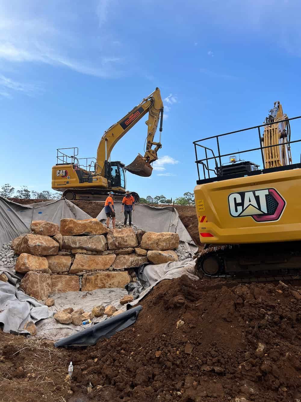 A Cat Excavator Is Moving Rocks On A Construction Site — J & M Bashforth & Sons In Brunswick Heads, NSW