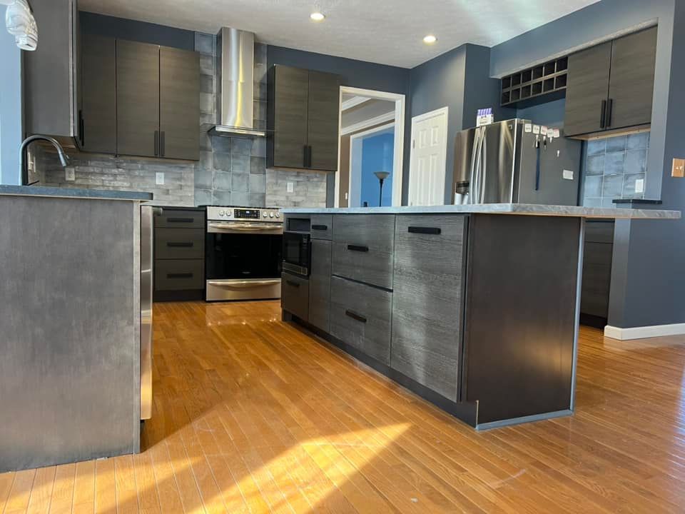 kitchen remodel by obringers featuring dark countertops with range hood, multiple backsplash materials, and dark blue wall