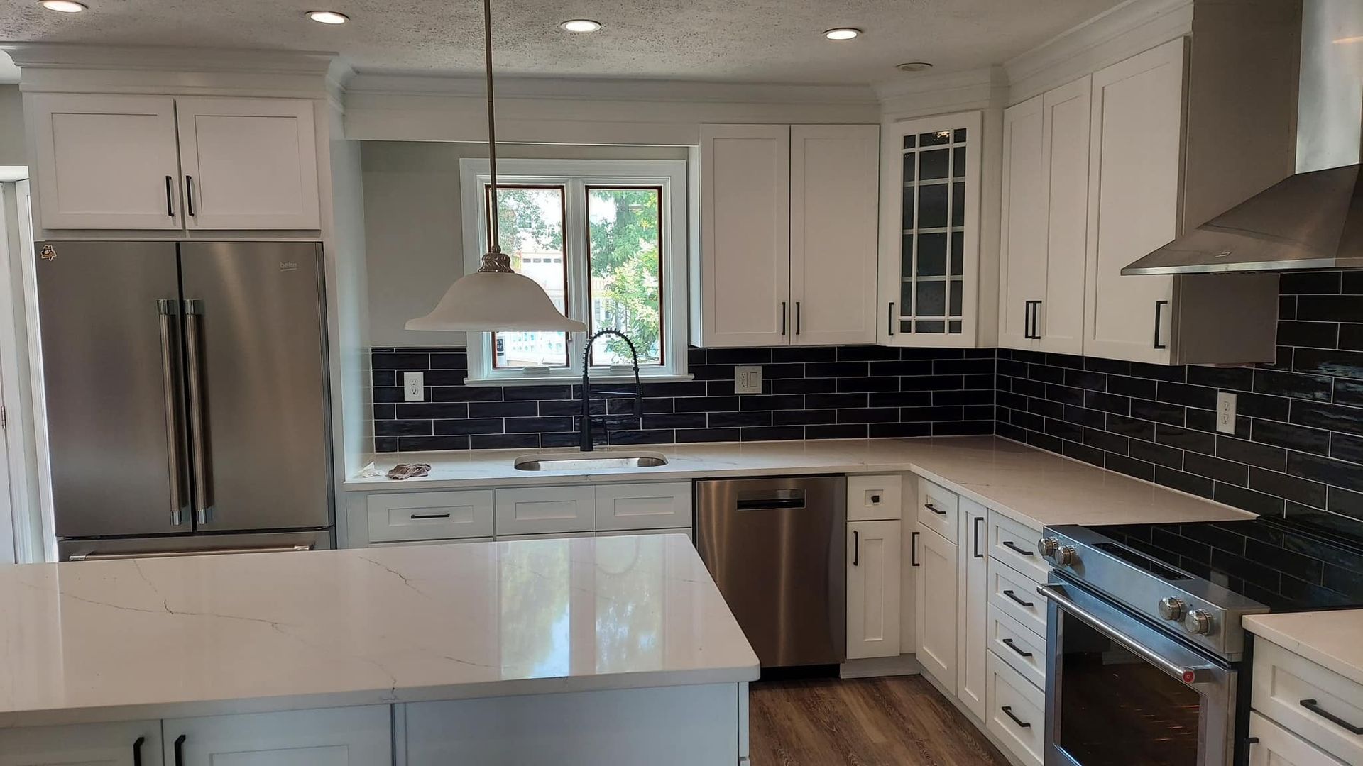 kitchen remodeling project by obringers with white shaker style cabinety and white granite countertops framed by a dark tile backsplash