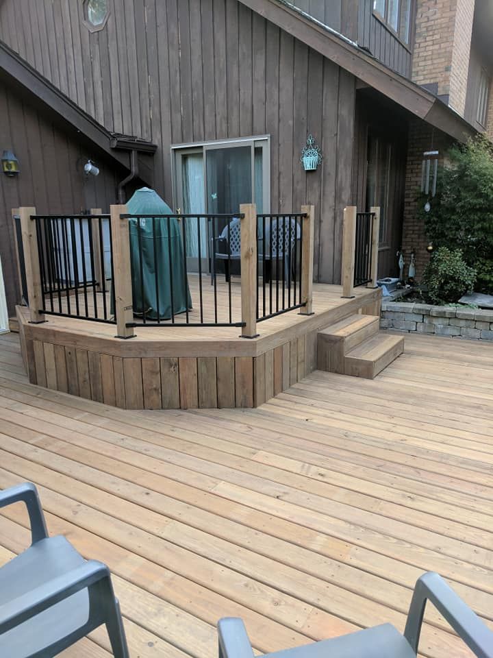 Wooden deck with a raised platform, black railing, and steps leading down.