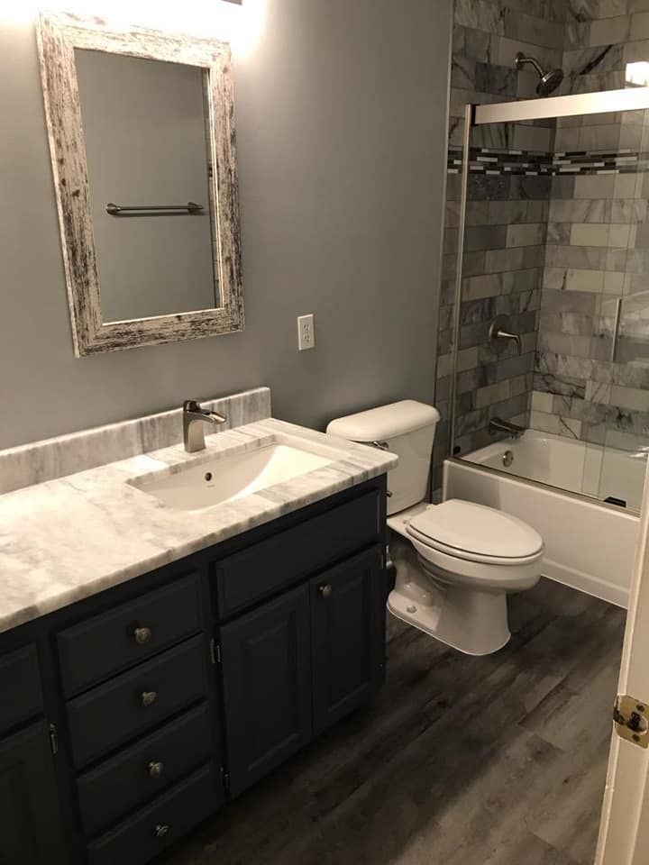 Bathroom with gray walls, dark cabinets, marble countertop, toilet, shower, and distressed mirror.