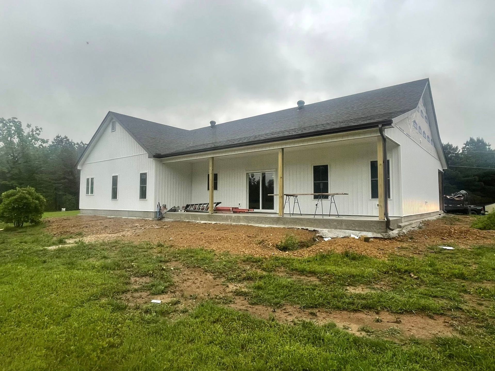 White house under construction with dark roof and porch, overcast sky.
