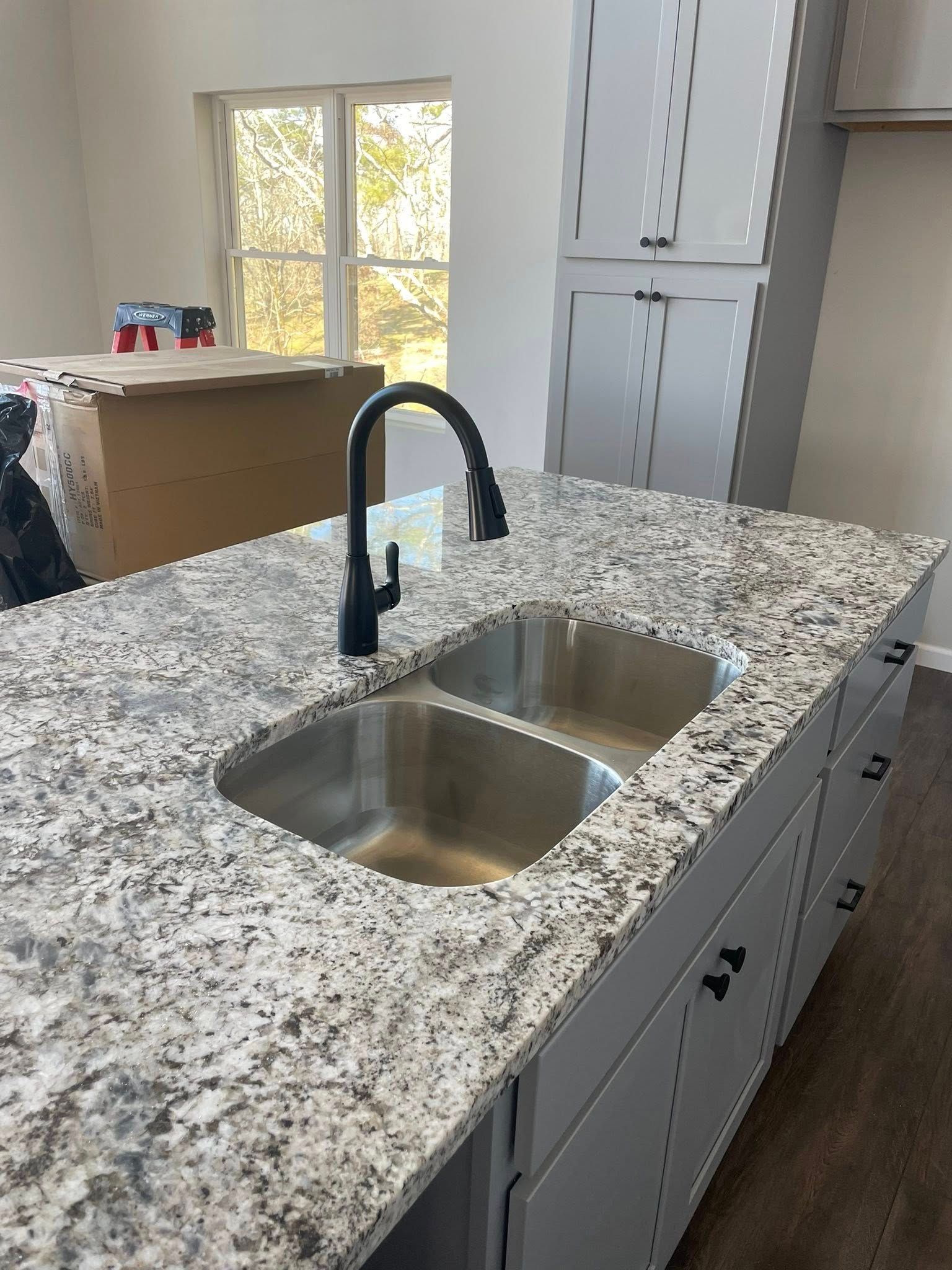 Kitchen island with stainless steel sink, granite countertop, and dark faucet. Grey cabinets below.