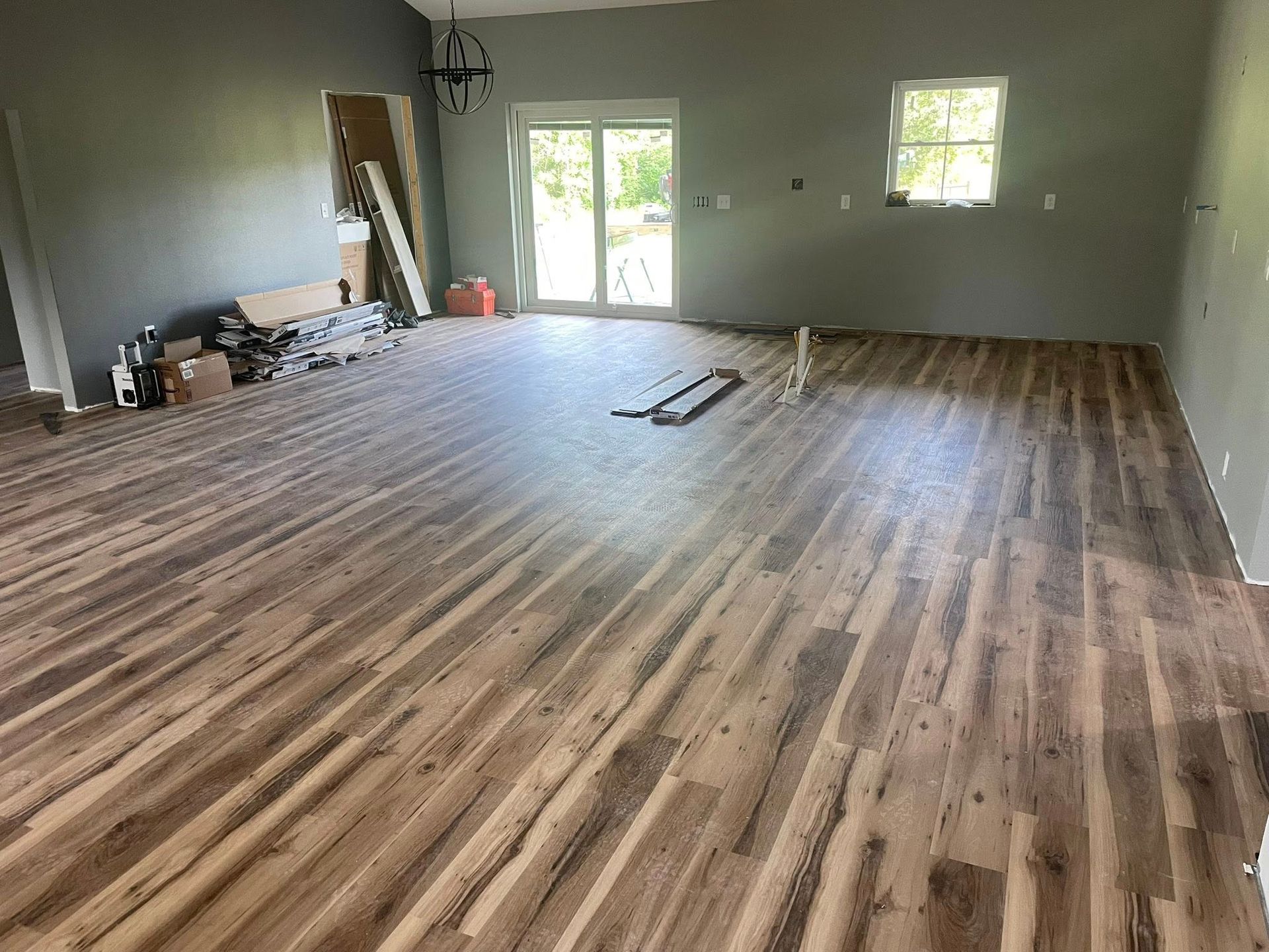 Newly installed wood-look flooring in a mostly empty room with gray walls and a sliding glass door.