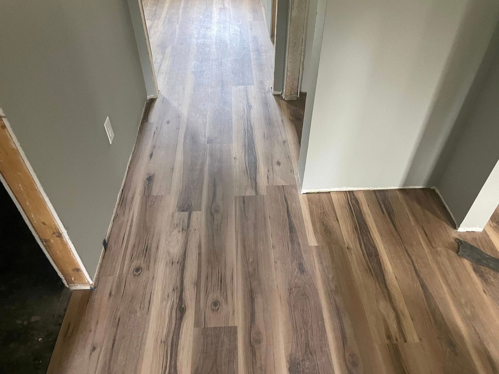 Hallway with light brown wood-look flooring, gray walls, and open doorways.