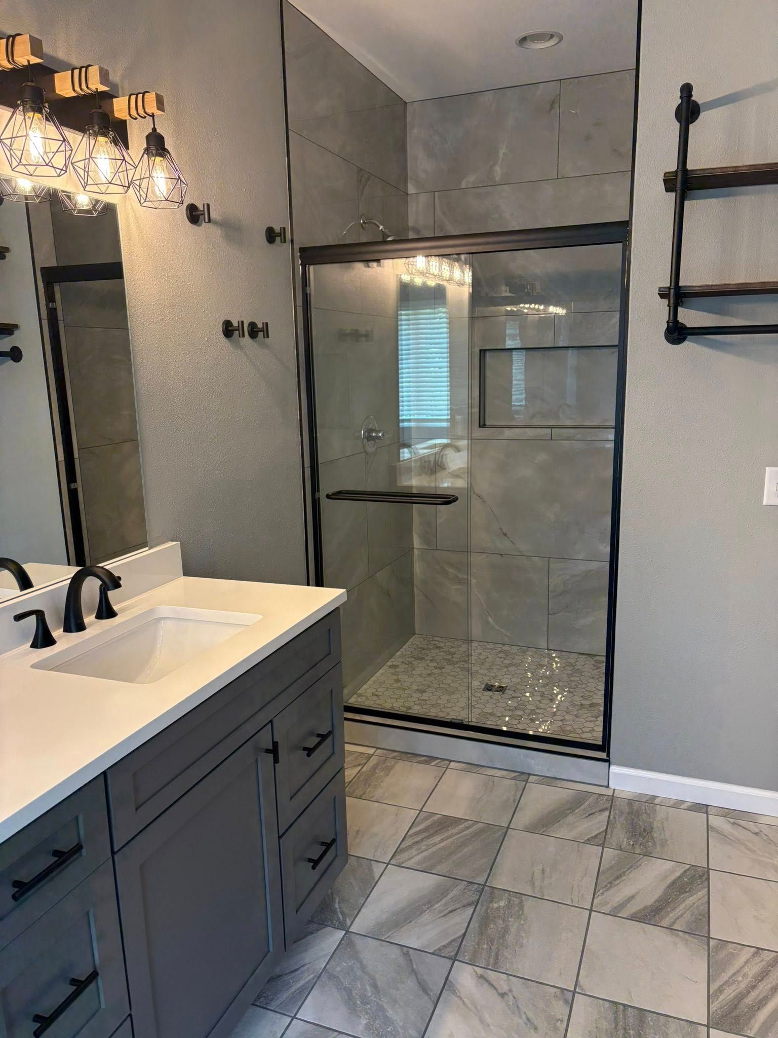 Bathroom with gray vanity, glass shower, gray tile floor and walls, black fixtures.