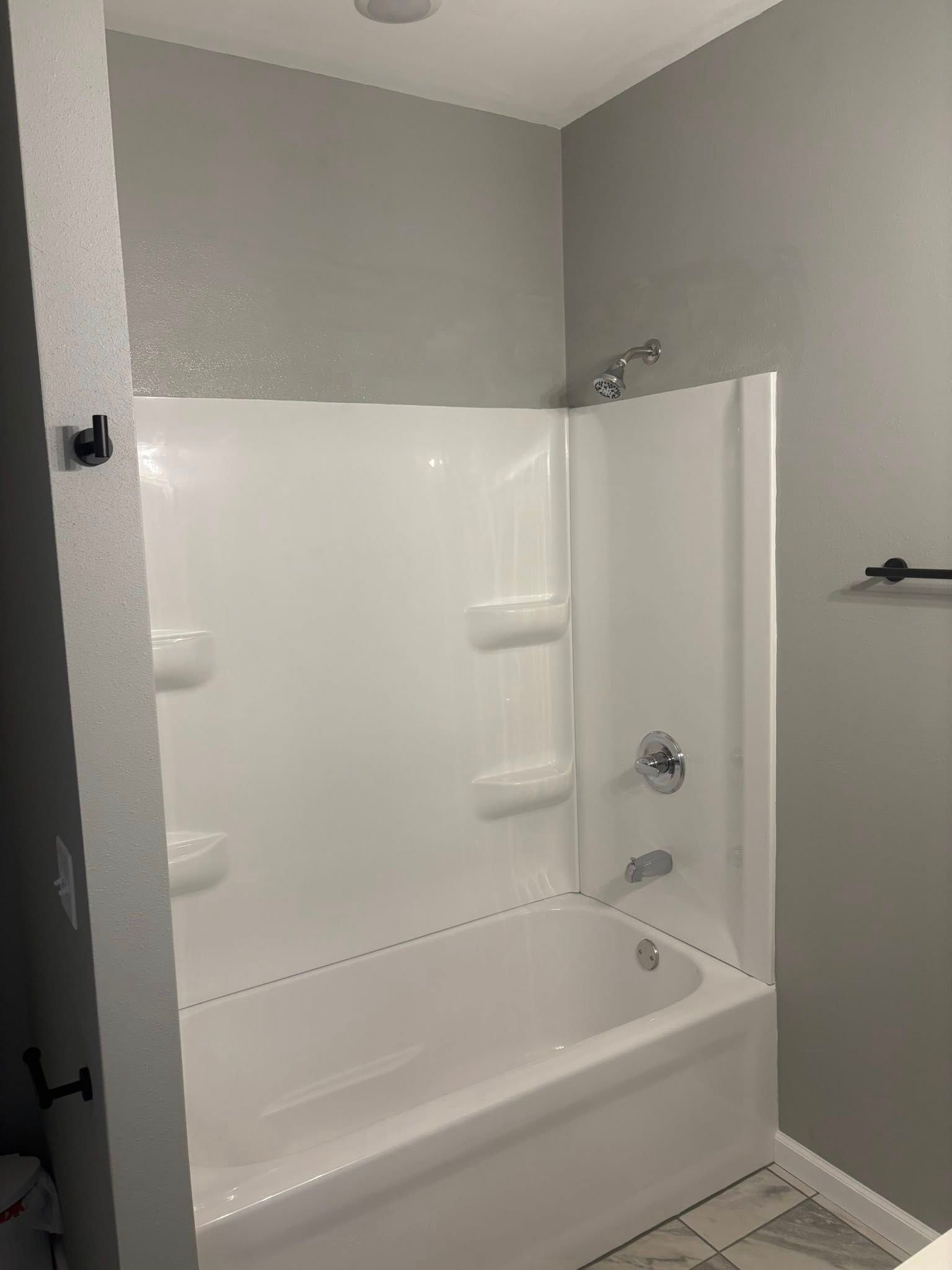 White bathtub with shower fixtures, gray walls, and a black towel rack.