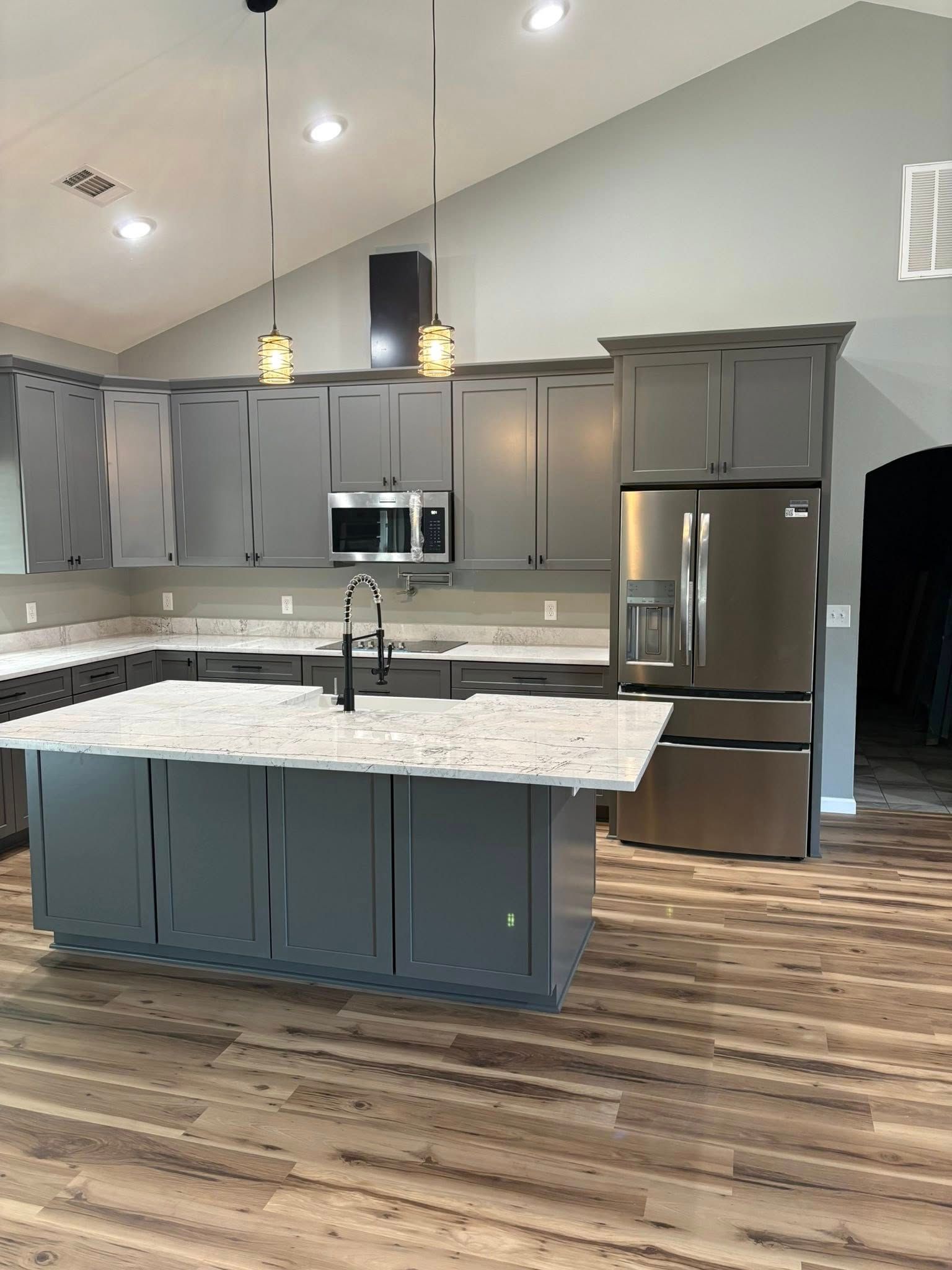 Gray kitchen with island, cabinets, and stainless steel refrigerator. Light wood-look floor.