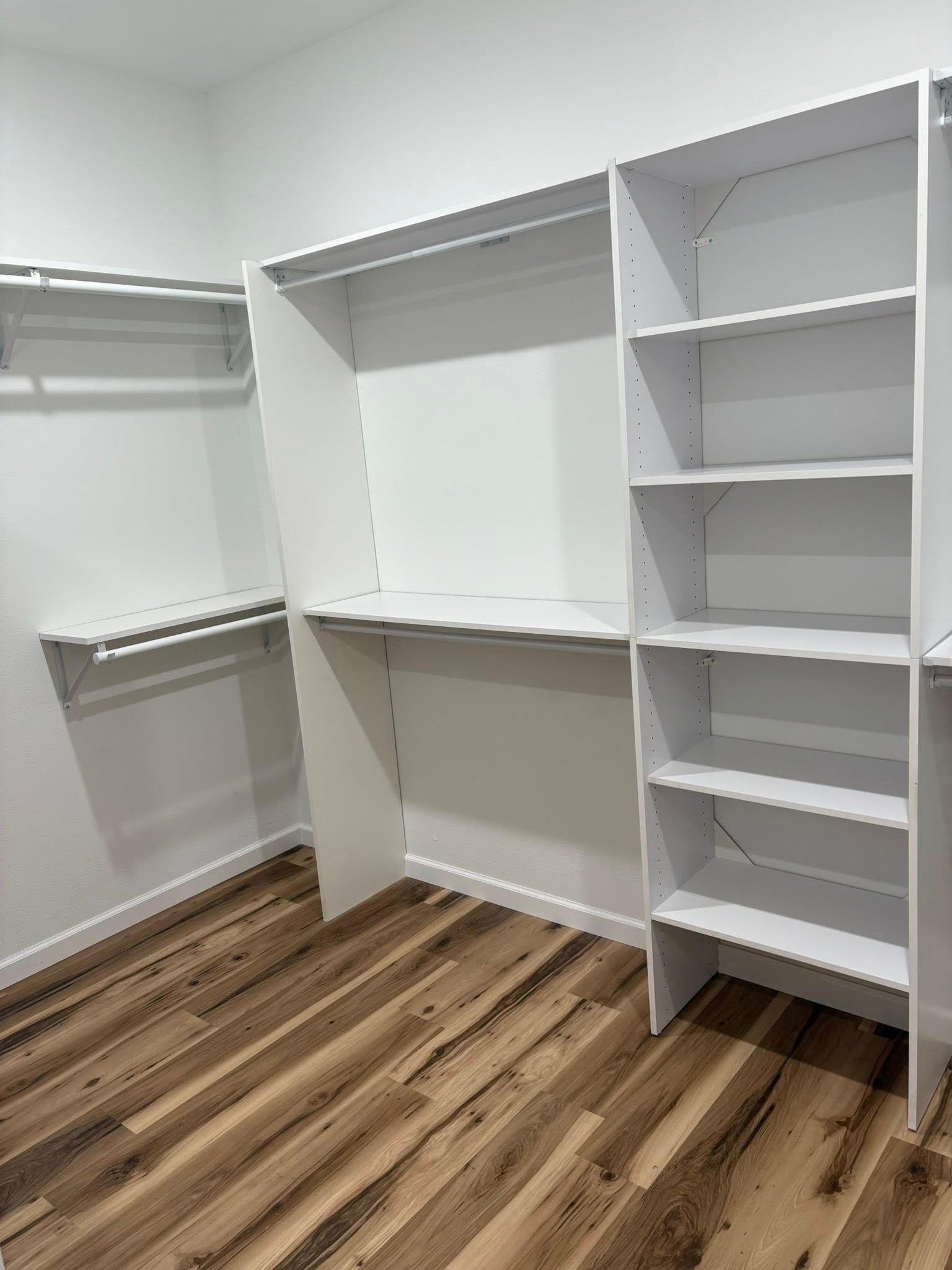 White closet with shelving and hanging rods against wood-look flooring.
