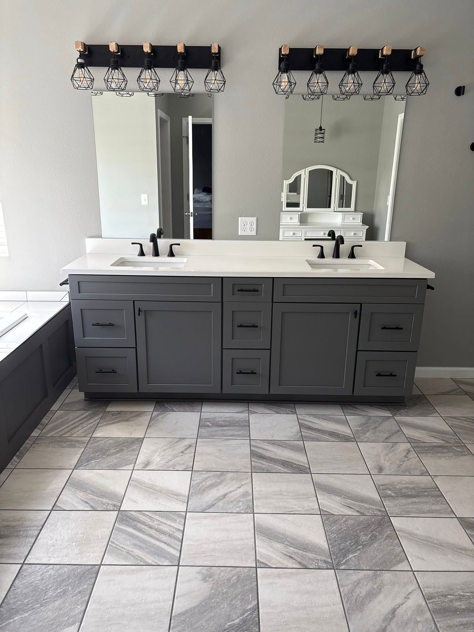 Gray bathroom vanity with two sinks and mirrors above. Gray and white patterned floor.