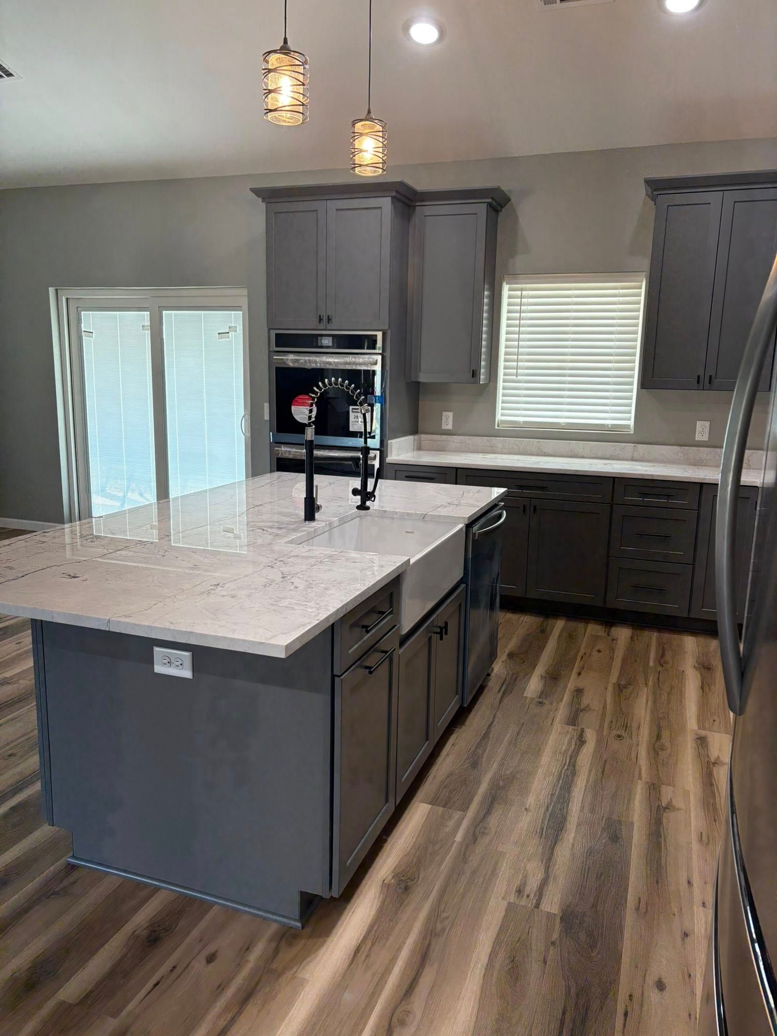 Gray kitchen with island, granite countertops, dark cabinets, wood floors, and pendant lights.