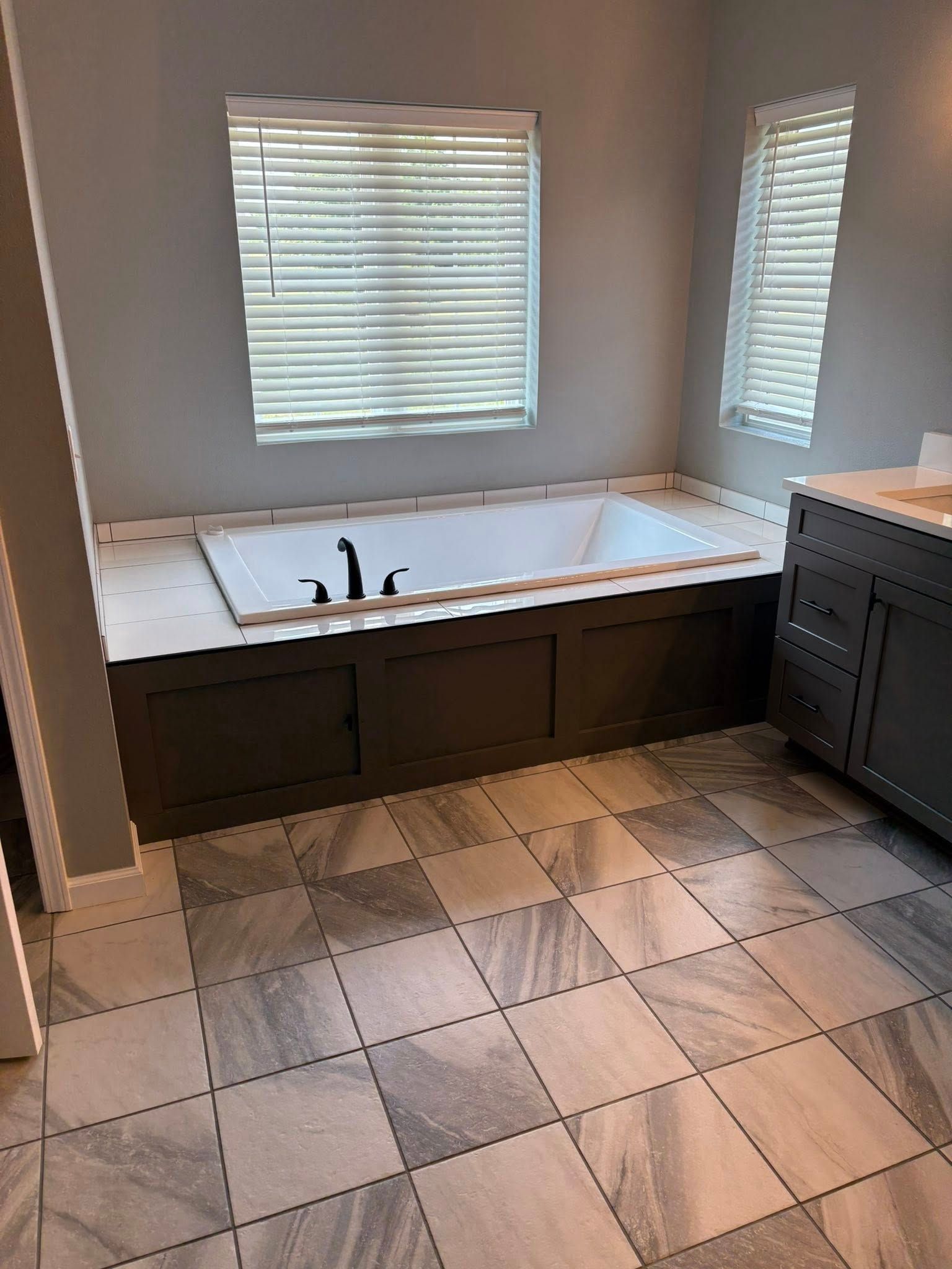 Bathroom with a built-in dark tub, gray tile flooring, and a gray vanity.