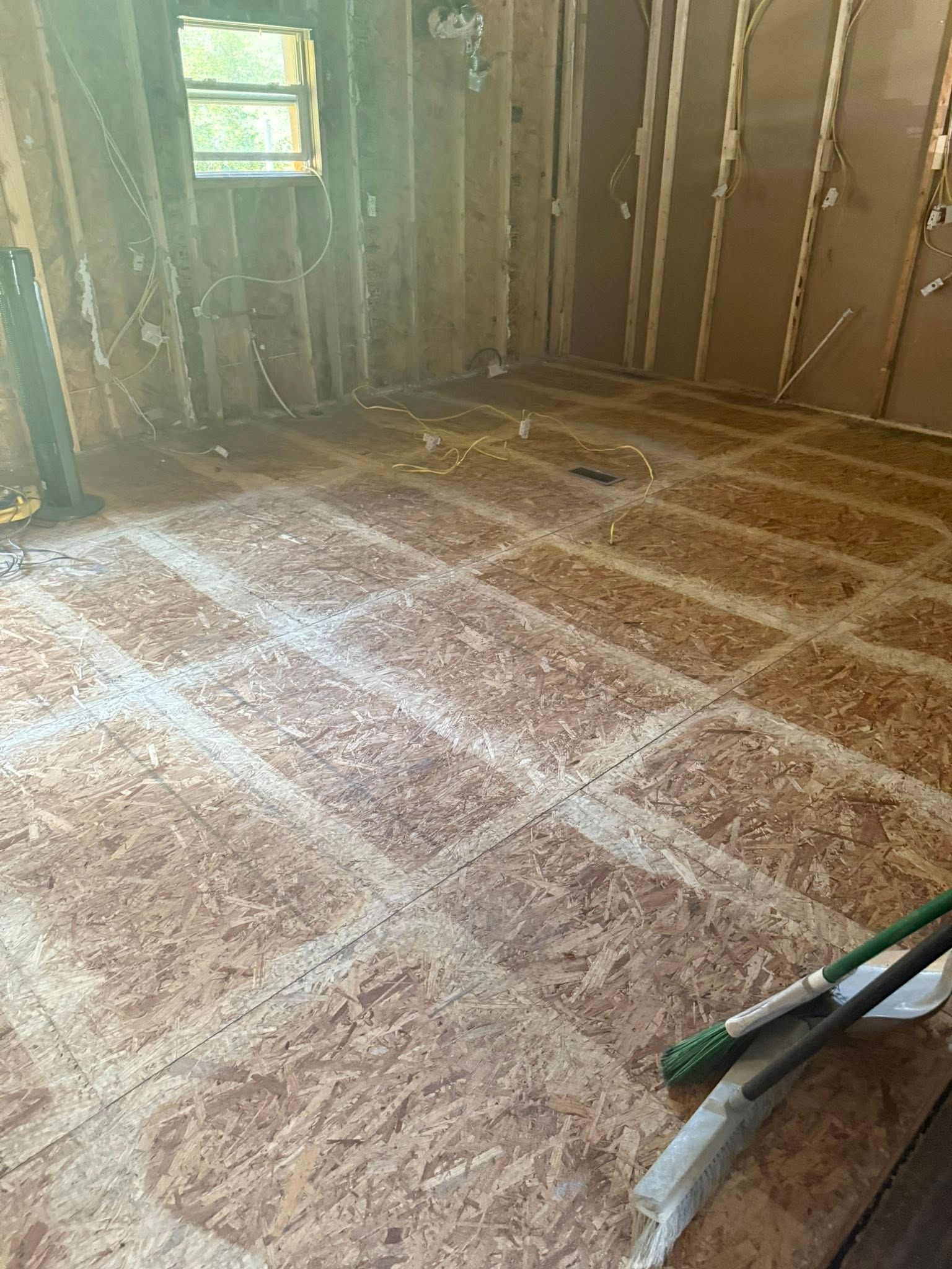 Room with exposed wooden floorboards and wall framing; tools lie on the floor.