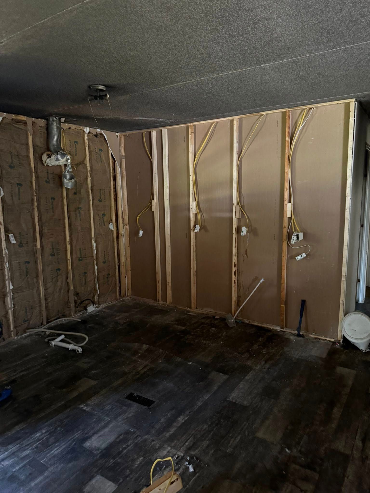 Interior room gutted, exposing studs and electrical wiring. Dark flooring and damaged ceiling.