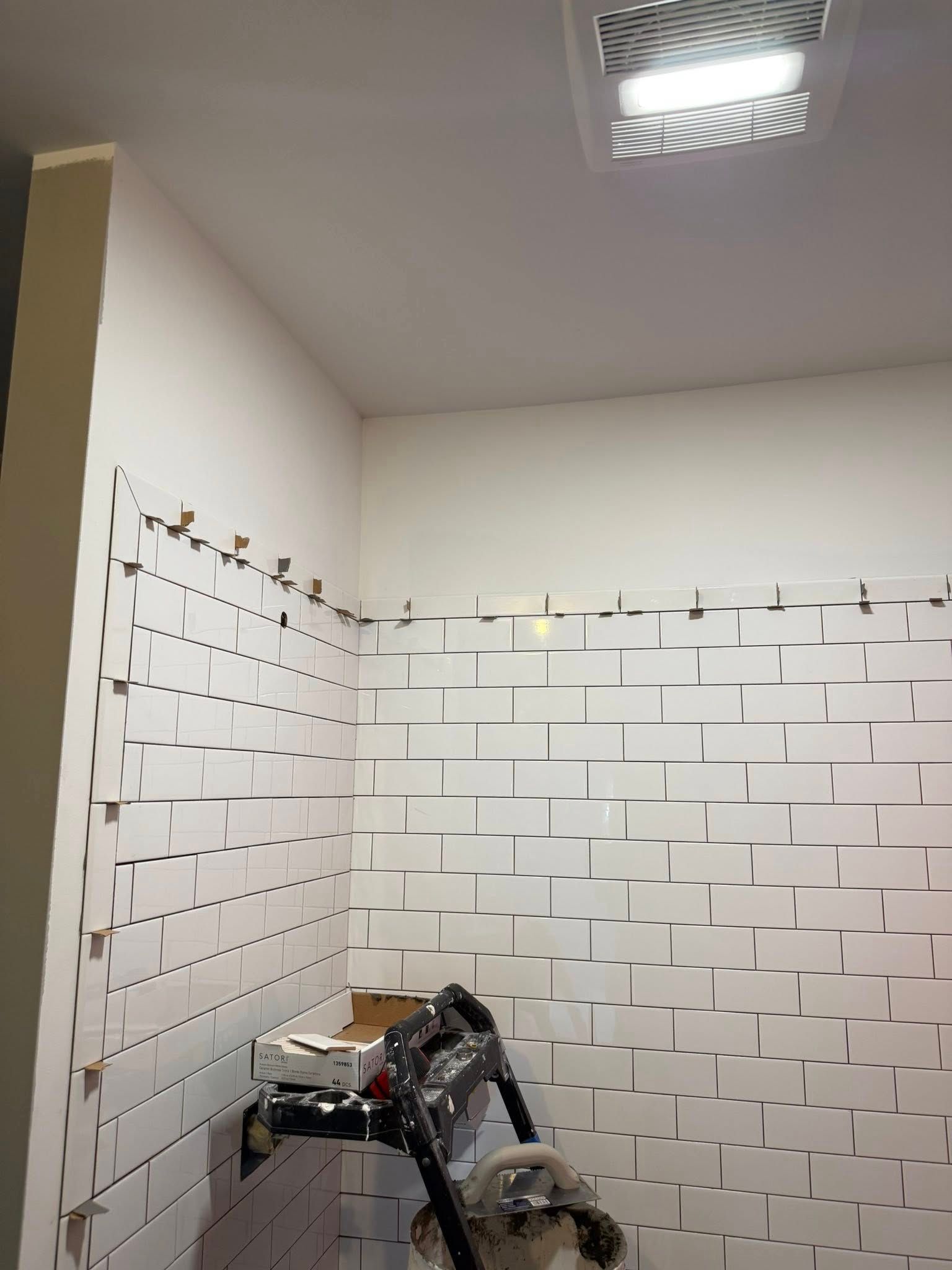 Bathroom under construction; white subway tile installation in progress.