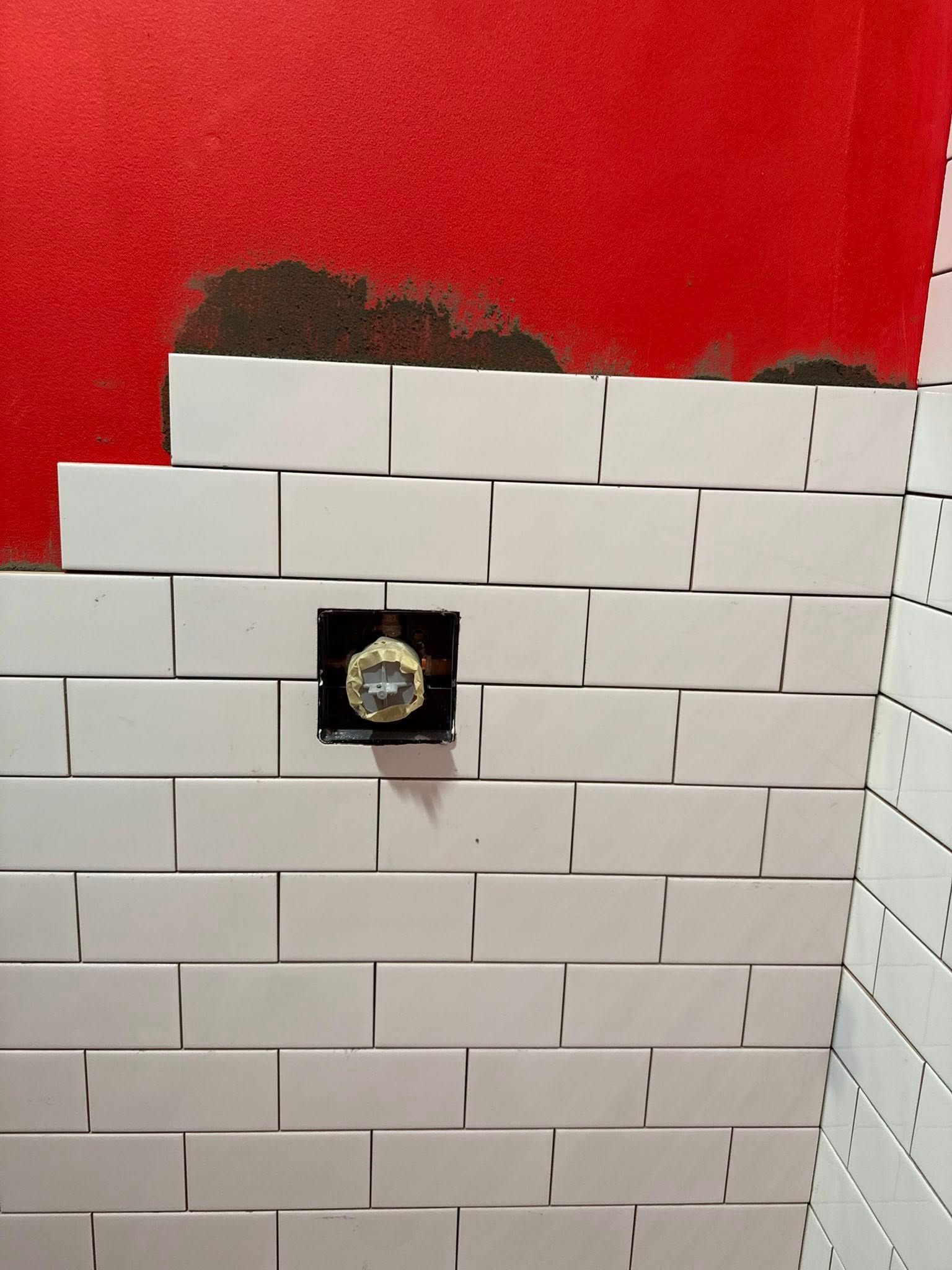 White subway tiles being installed on a red wall, with a plumbing fixture and corner tiling.