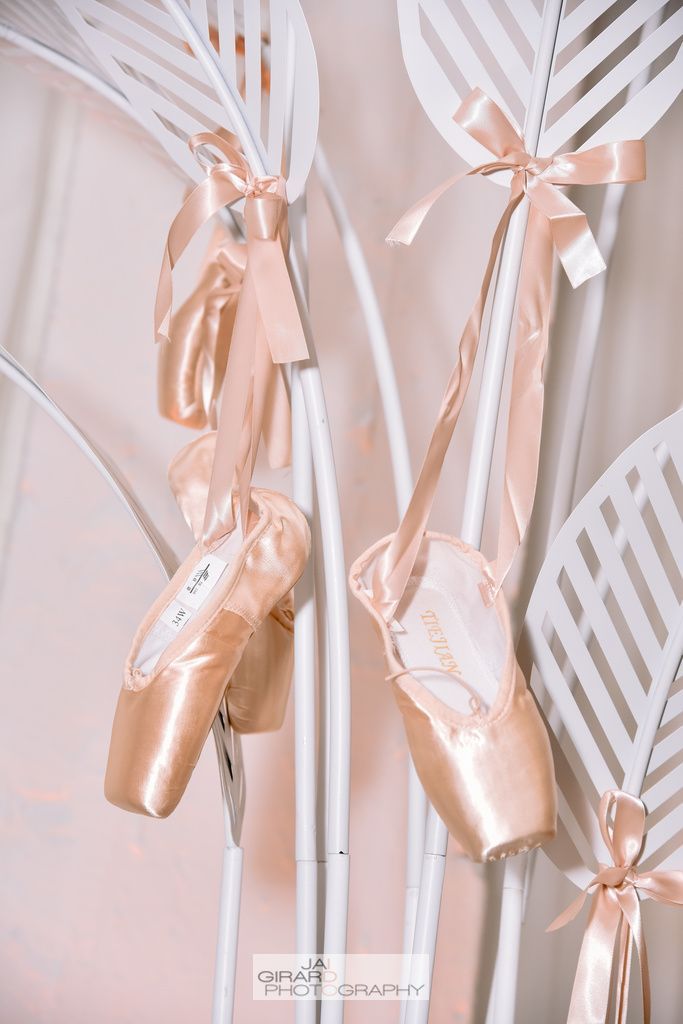 A pair of pink ballet shoes hanging from a white pole.