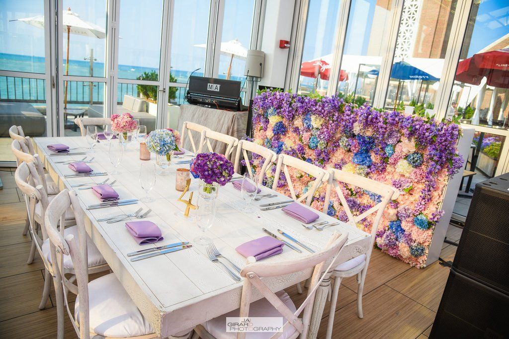 A long table with purple flowers on it is sitting in front of a wall of purple flowers.