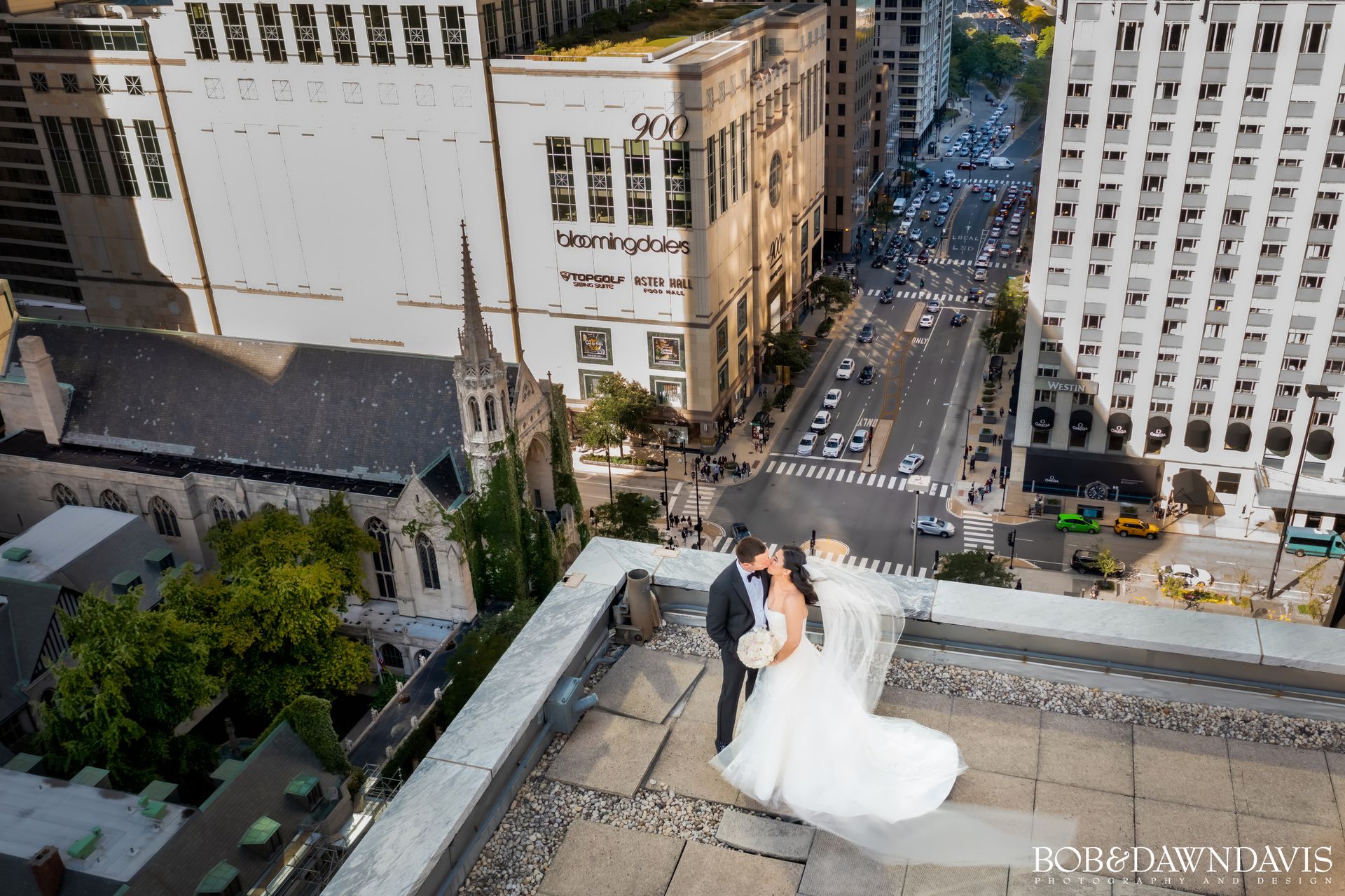 A bride and groom are kissing on the roof of a building