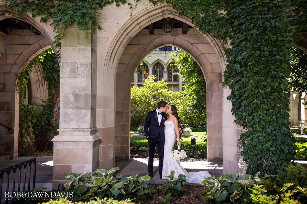 A bride and groom are kissing under a stone archway.