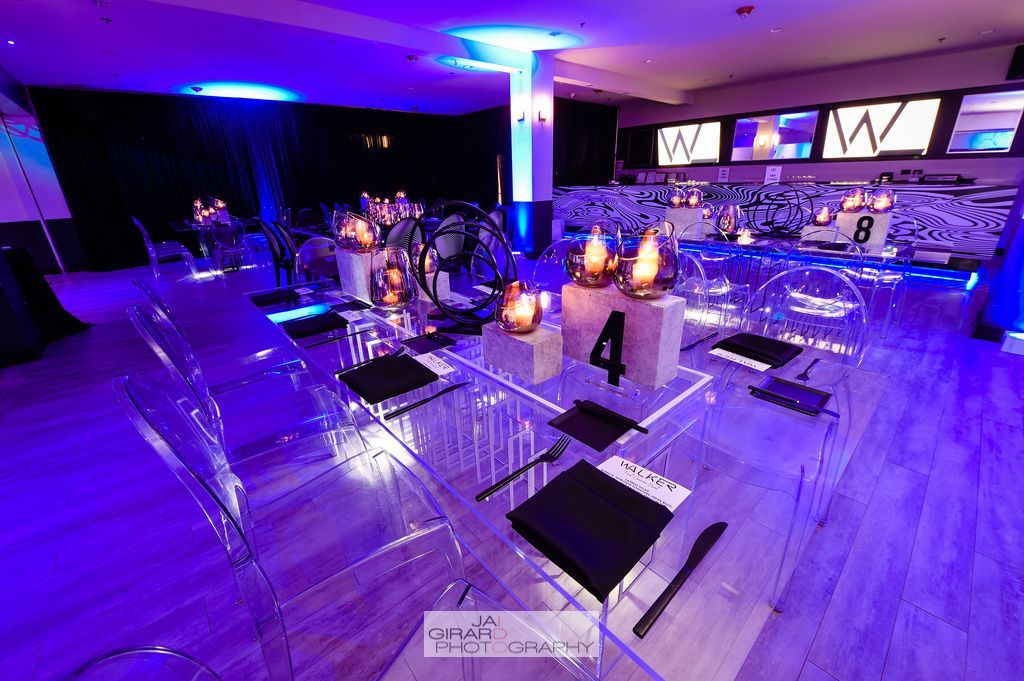 A room with a table and chairs set up for a party with purple lights.