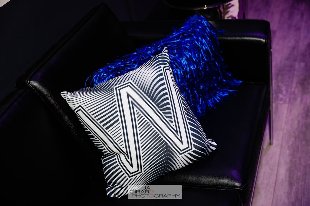 Two pillows with the letter w on them are sitting on a black couch.