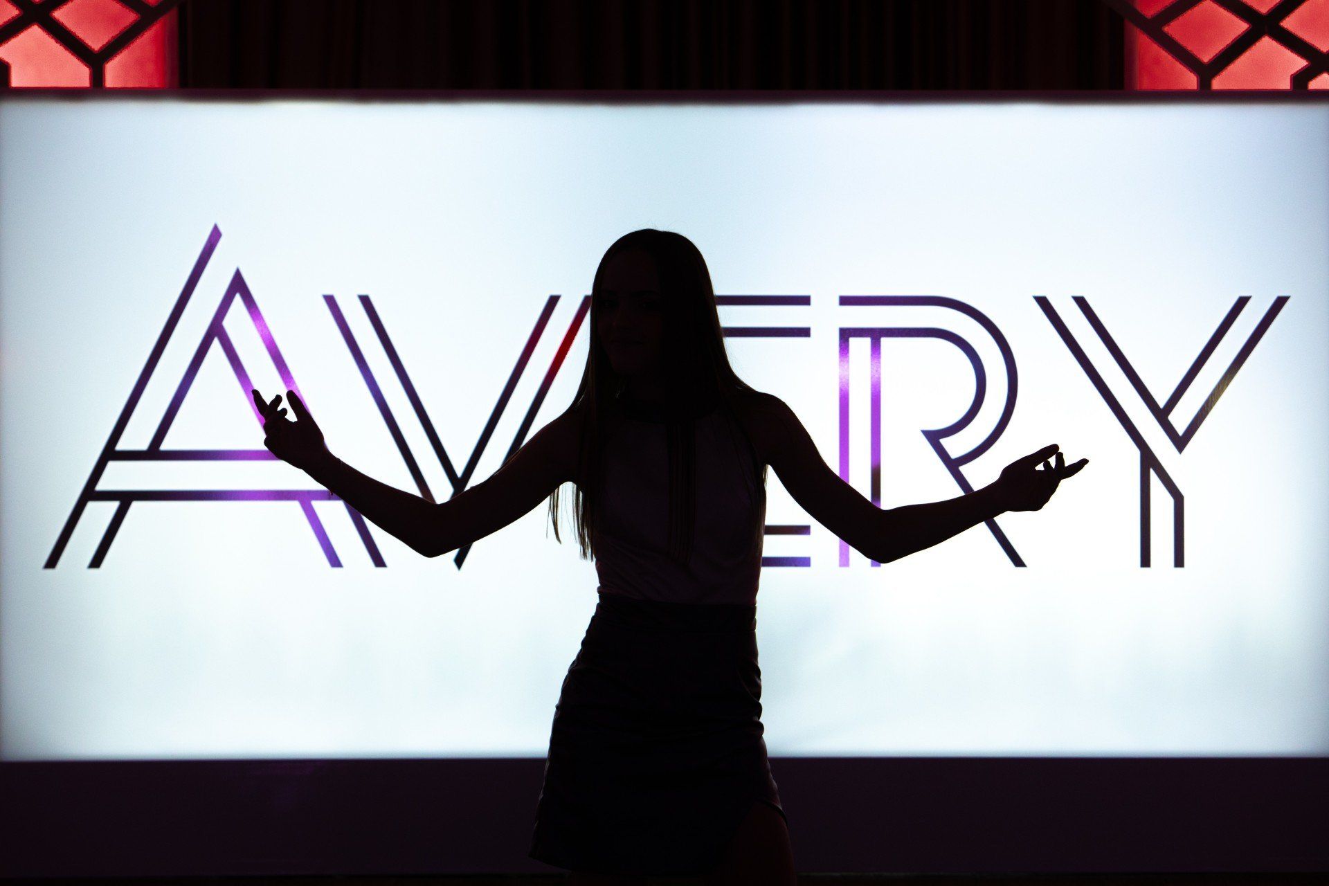 A woman is dancing in front of a sign that says avery