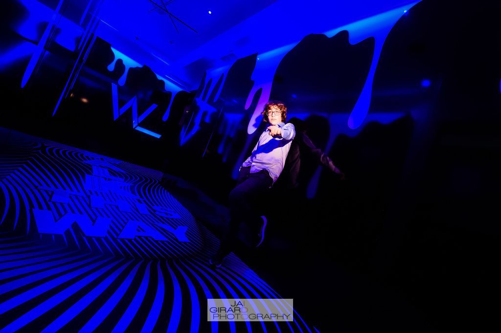 A man in a suit is dancing in a dark room with blue lights