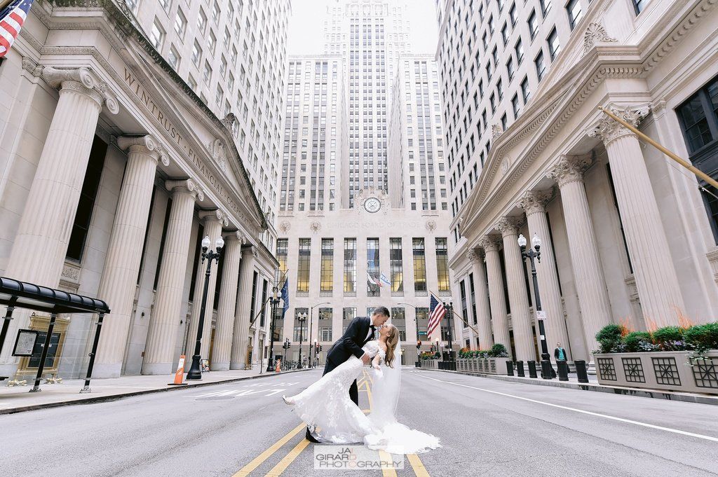 A bride and groom are kissing on the street in front of a large building.