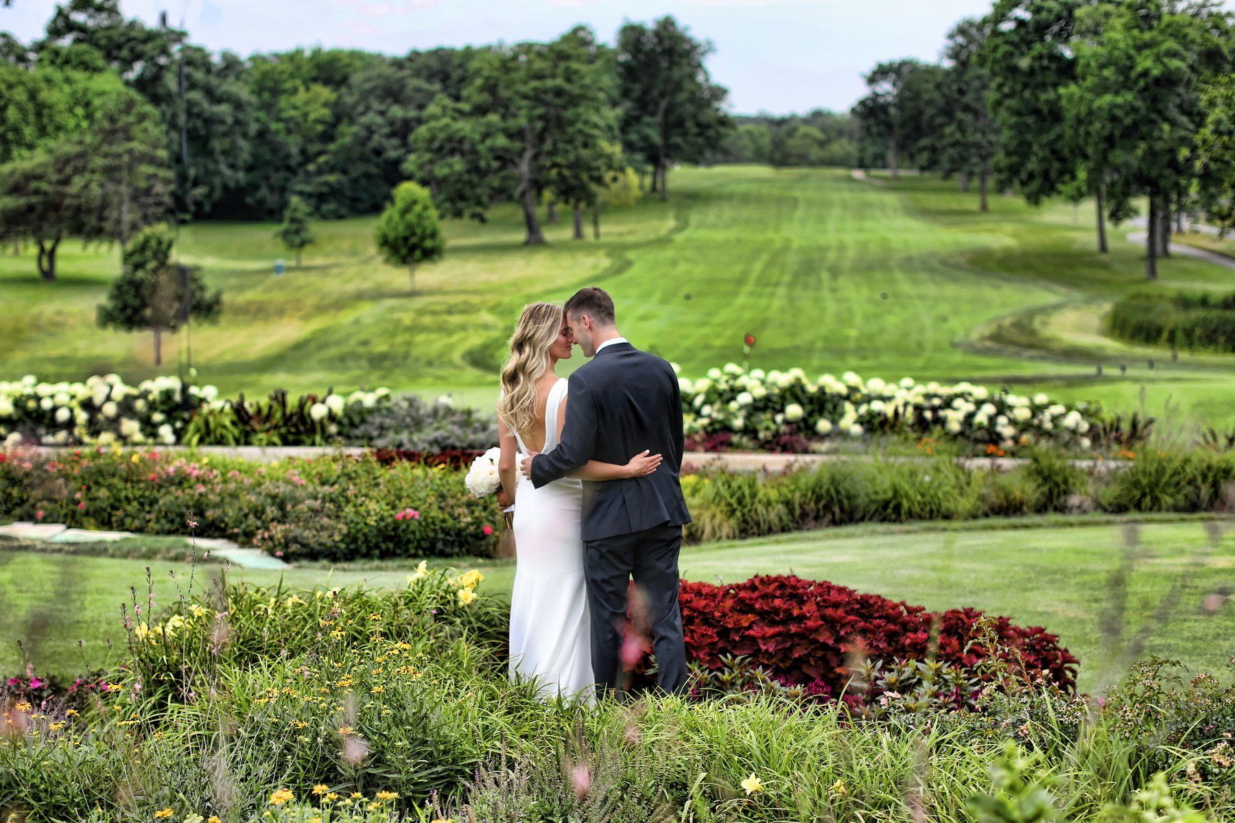 A bride and groom are standing in a garden in front of a golf course.