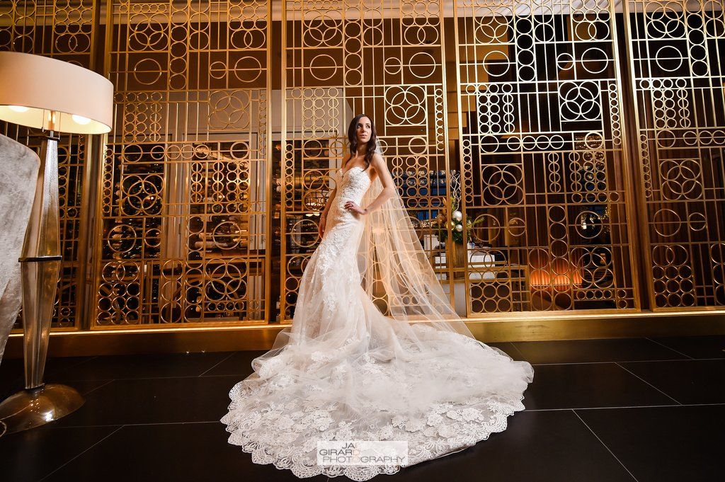 A woman in a wedding dress and veil is standing in front of a gold wall.