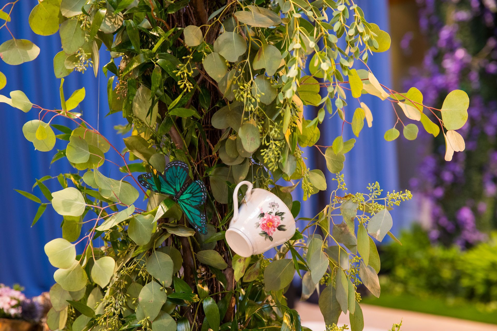 A tea cup is hanging from a tree with flowers and leaves.