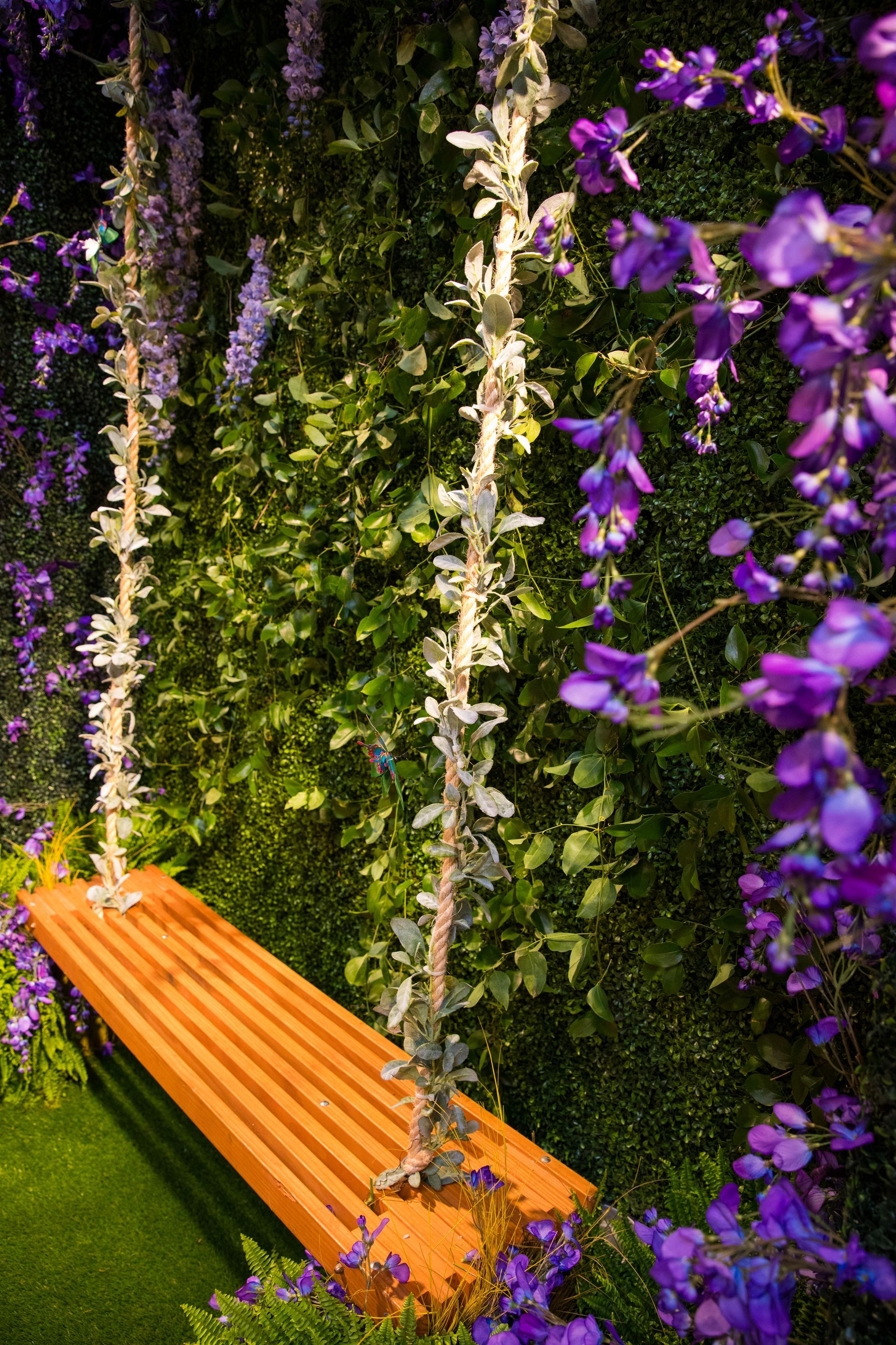 A wooden bench is sitting in front of a wall of purple flowers.