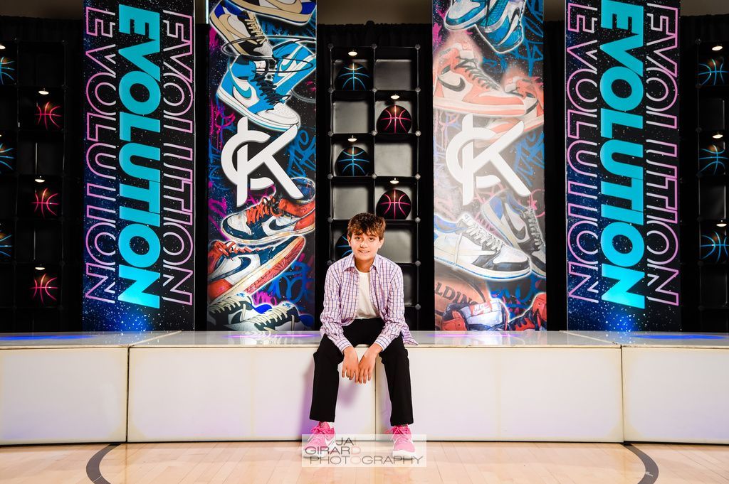 A young boy is sitting on a bench in front of a wall that says evolution.