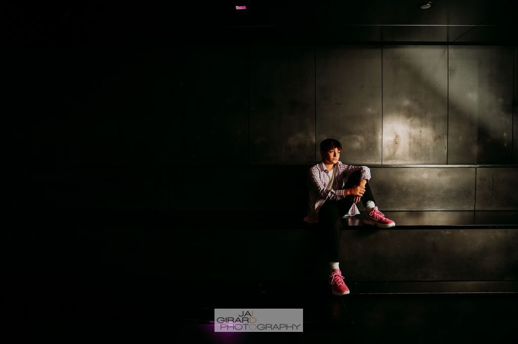 A man is sitting on a bench in the dark looking at his phone.