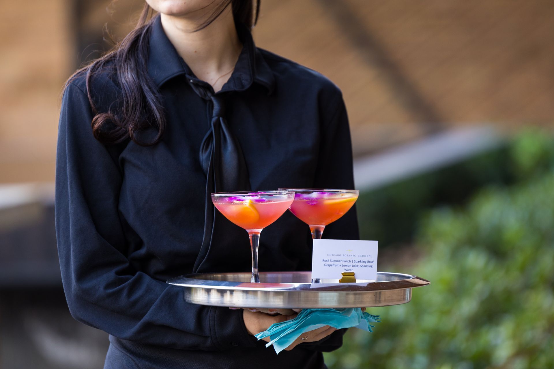A woman is holding a tray with two cocktails on it.