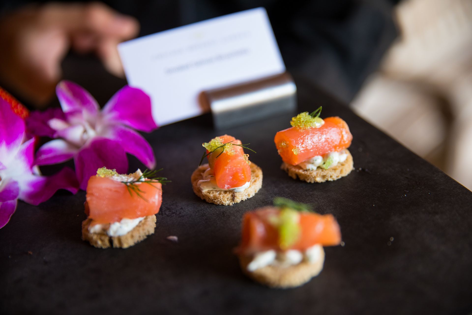A person is holding a business card next to a tray of appetizers.